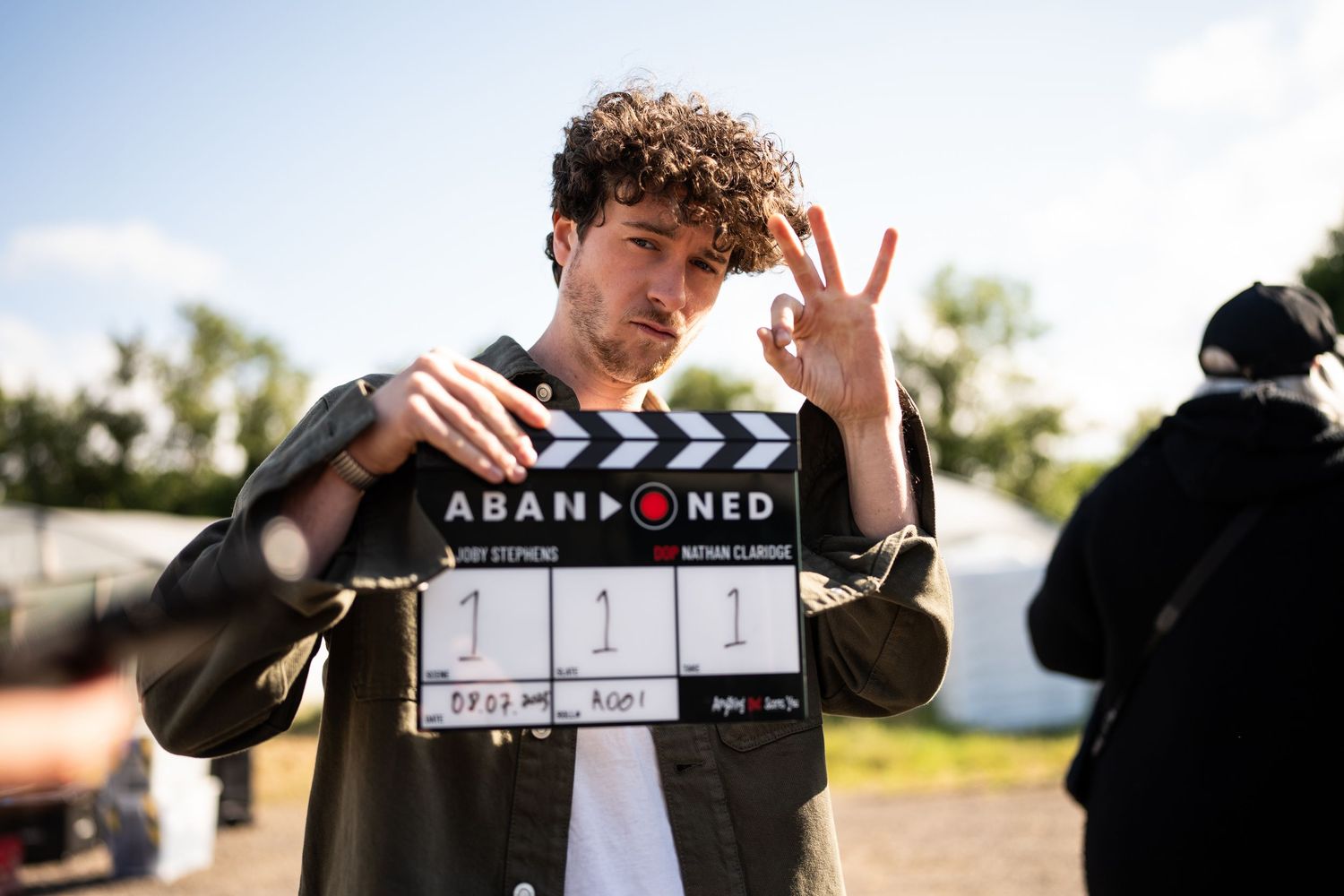 A young man holds an Abandoned film clapperboard on a movie set outdoors.