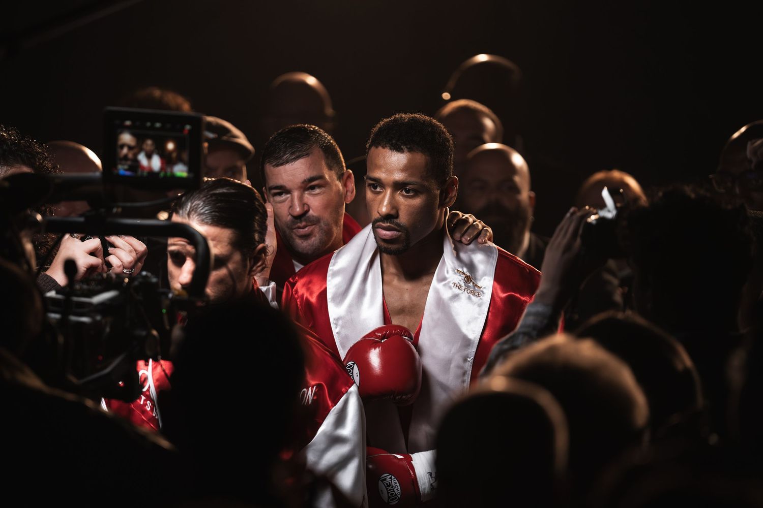 Boxer wrapped in white robe walking through crowd at professional boxing event.