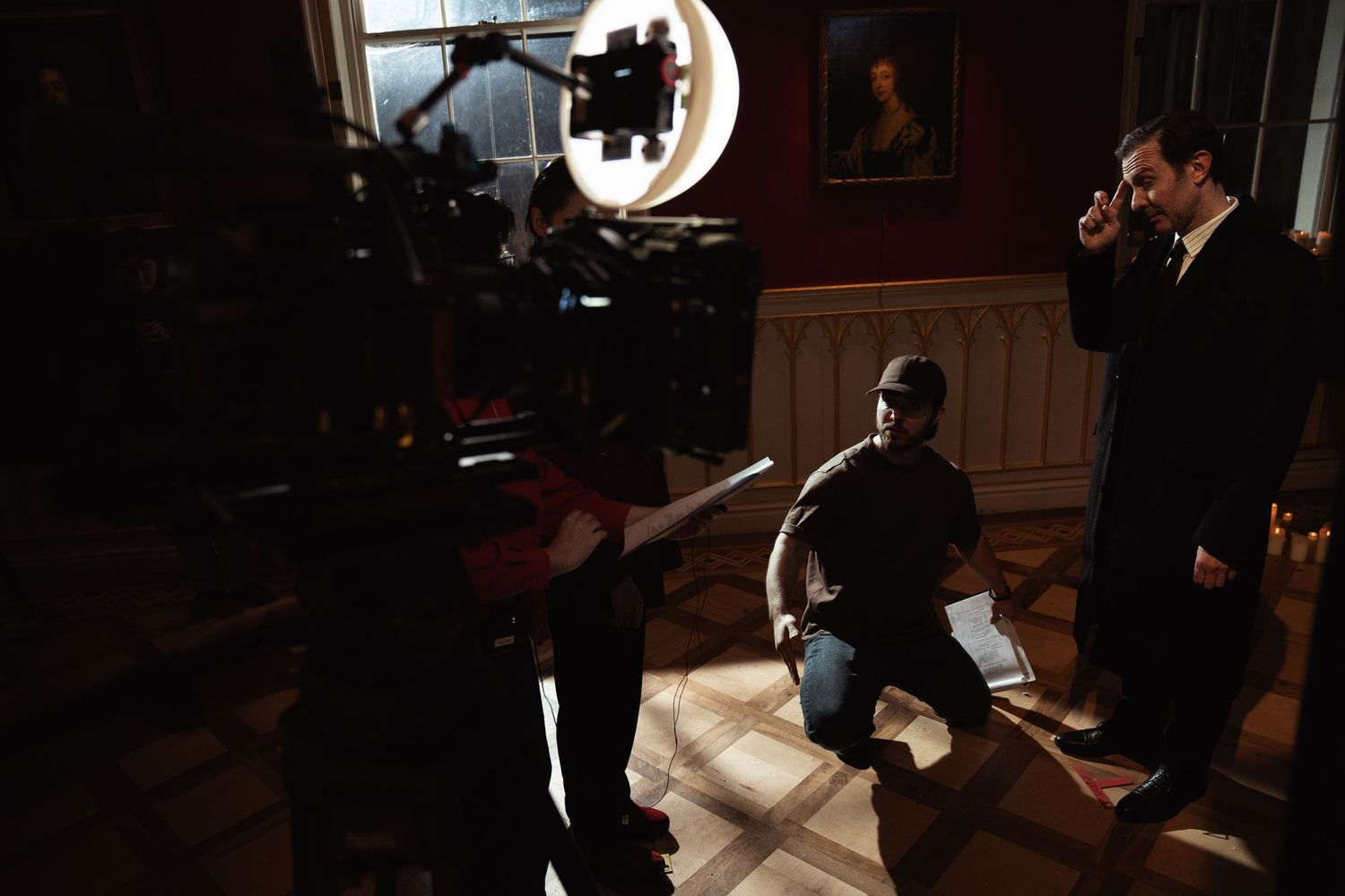 A film crew captures a scene inside an elegant room with a man in a suit speaking on a phone.