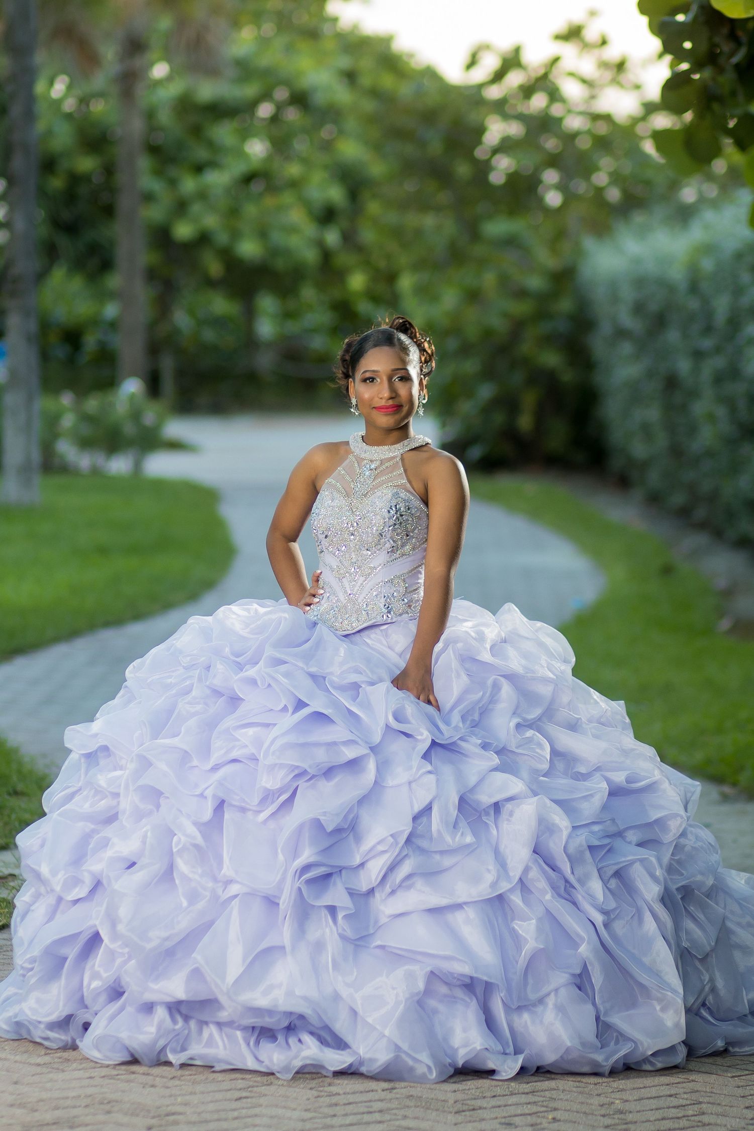 Young woman in lavender ball gown quinceanera dress with beaded bodice poses on garden pathway.