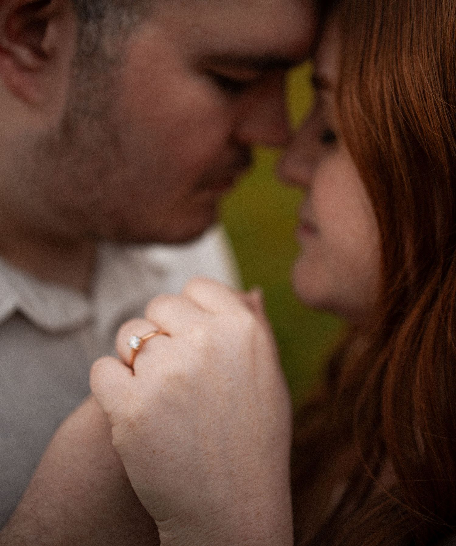 Soft focus romantic photo of couple touching foreheads, woman displaying diamond engagement ring on hand.