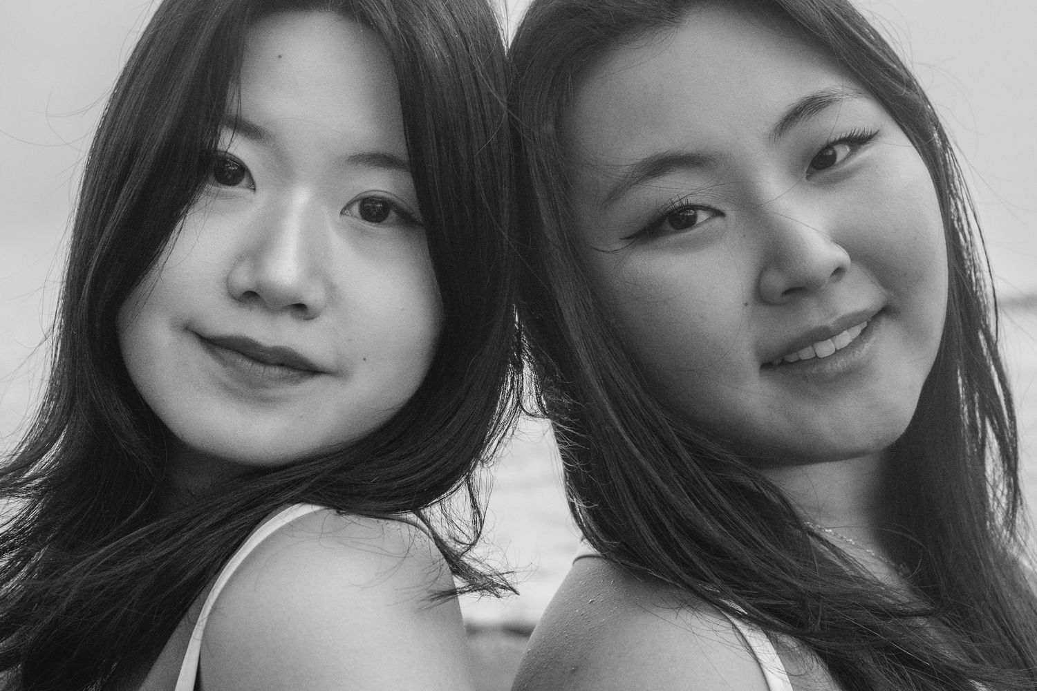 Black and white portrait of two smiling young Asian women posing closely together outdoors.