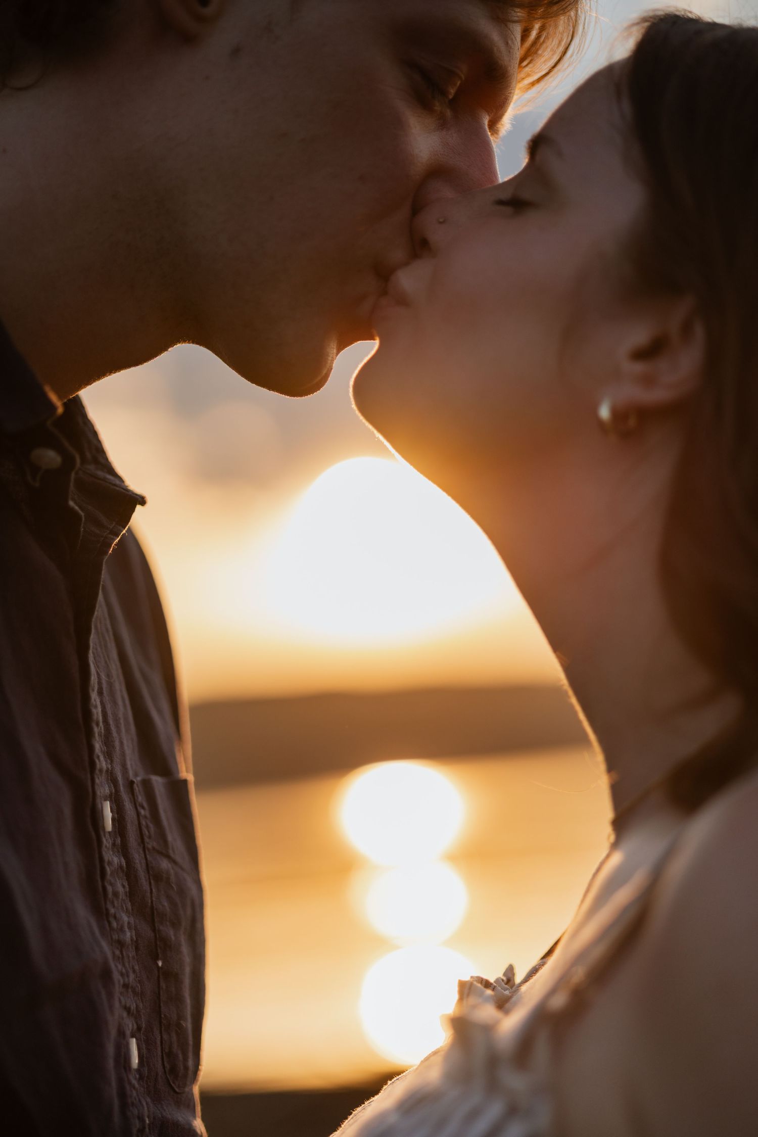Romantic couple sharing a kiss silhouetted against a golden sunset over water.