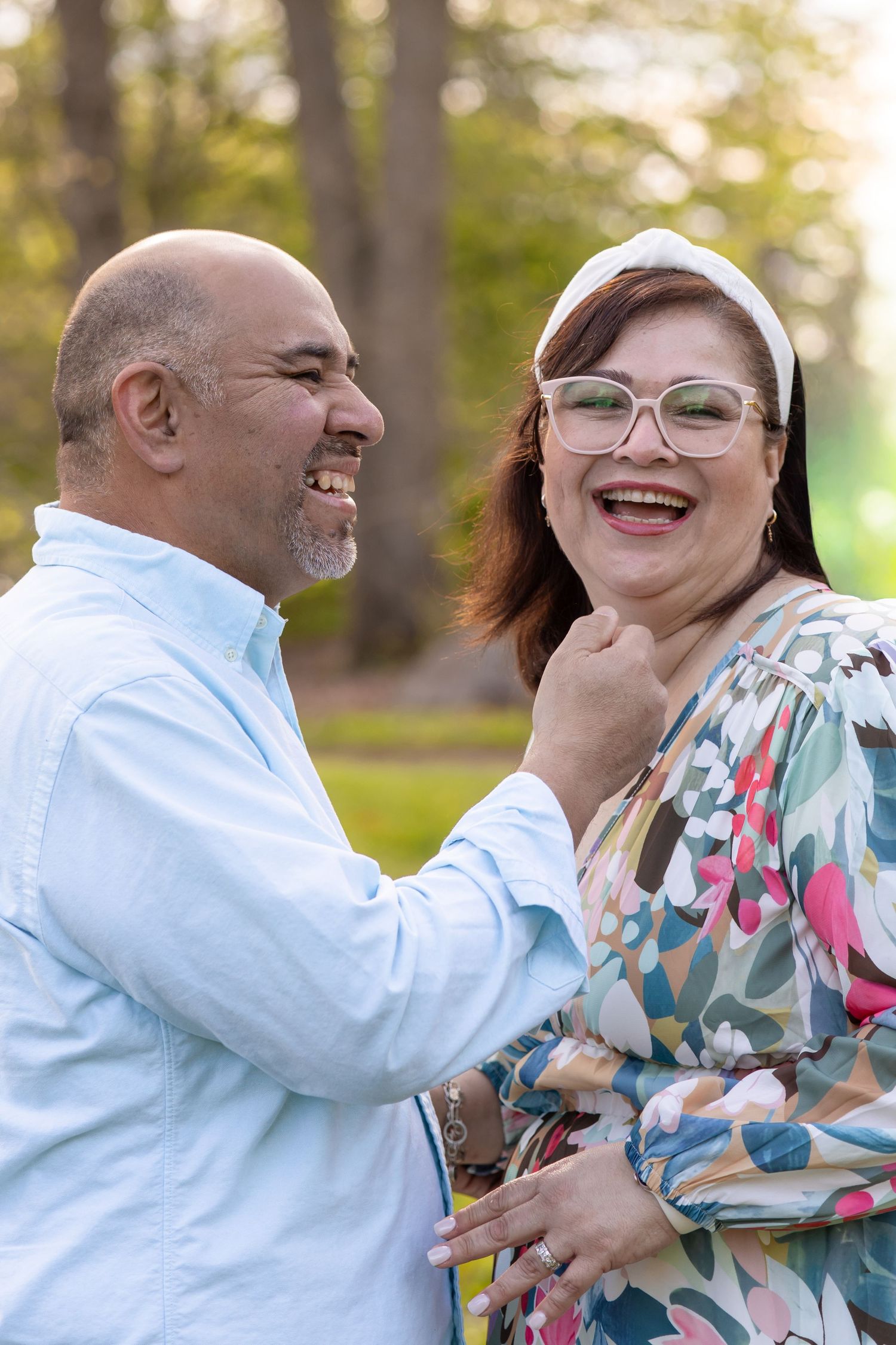 A laughing middle-aged couple enjoys a joyful moment together outdoors in a sunny park setting.
