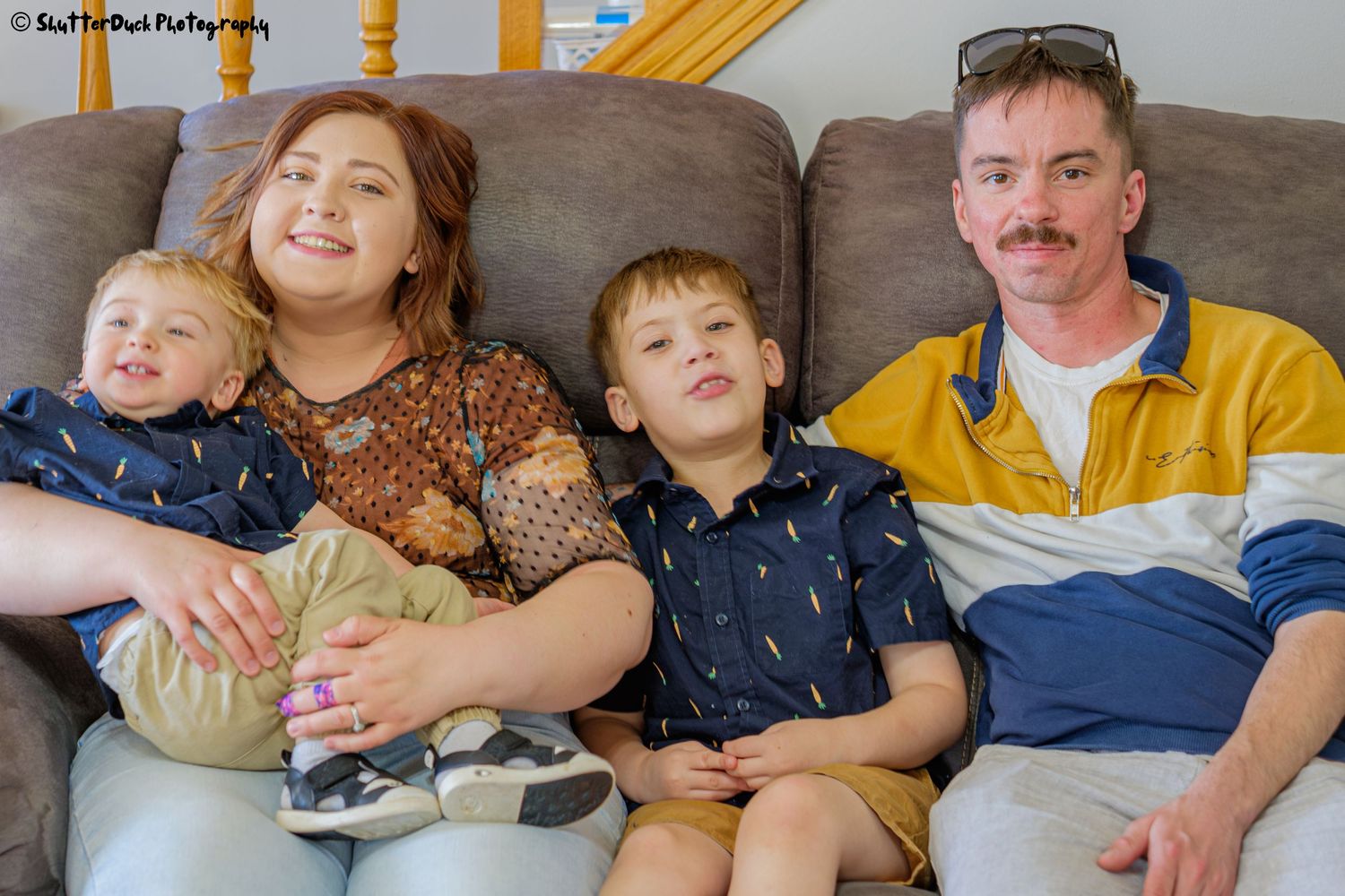 Family of four relaxing together on a gray couch, including two young boys and their parents.