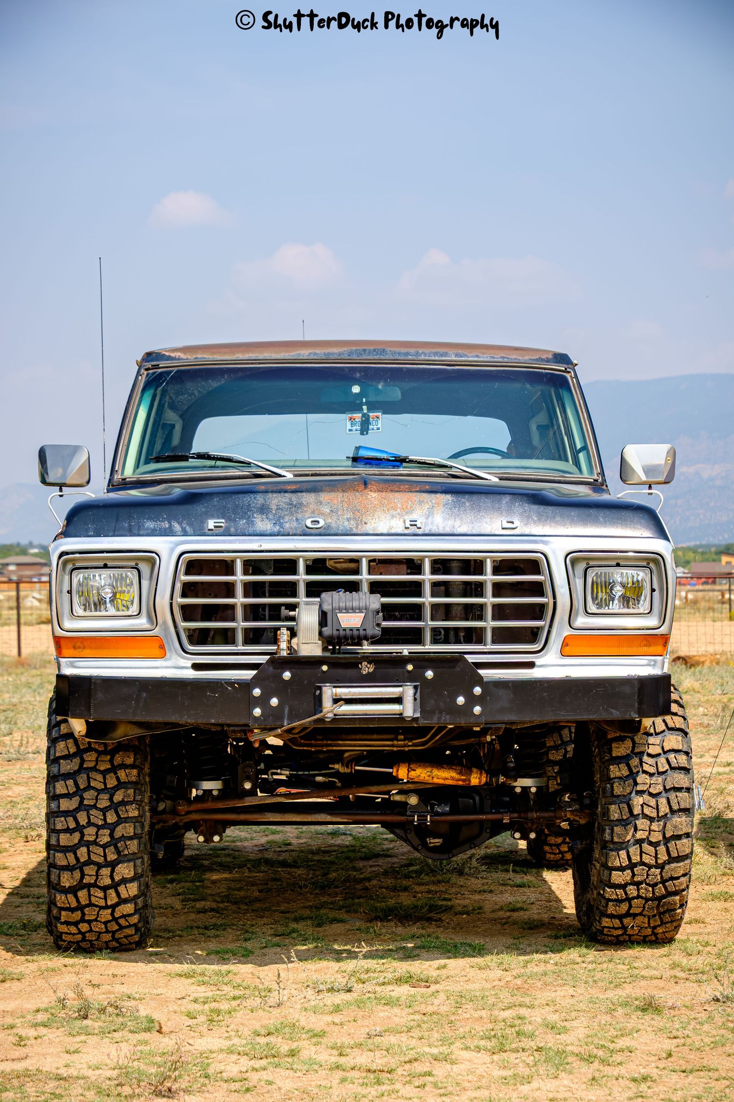 Front view of a lifted vintage Ford bronco with a winch bumper parked on dry dirt field.