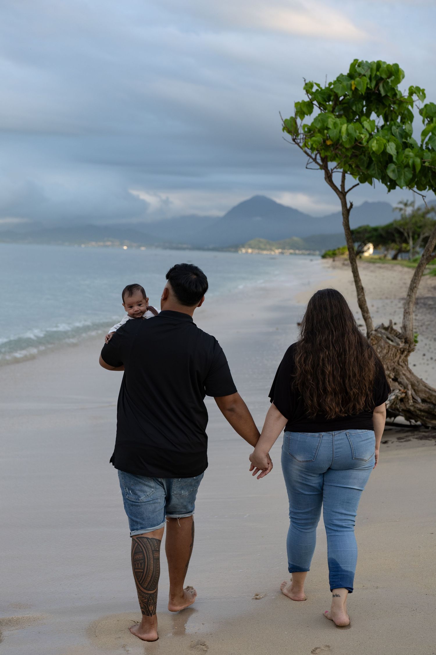 Family holding hands walking on Hawaii beach at sunset with baby.