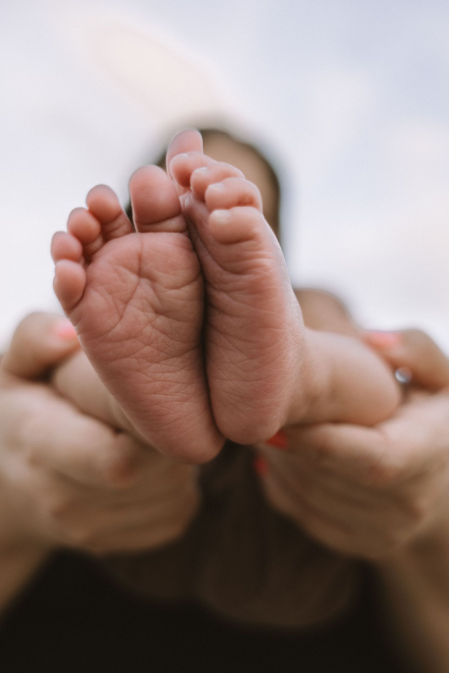 Parent tenderly holding tiny newborn baby feet toward camera against a soft sky background.