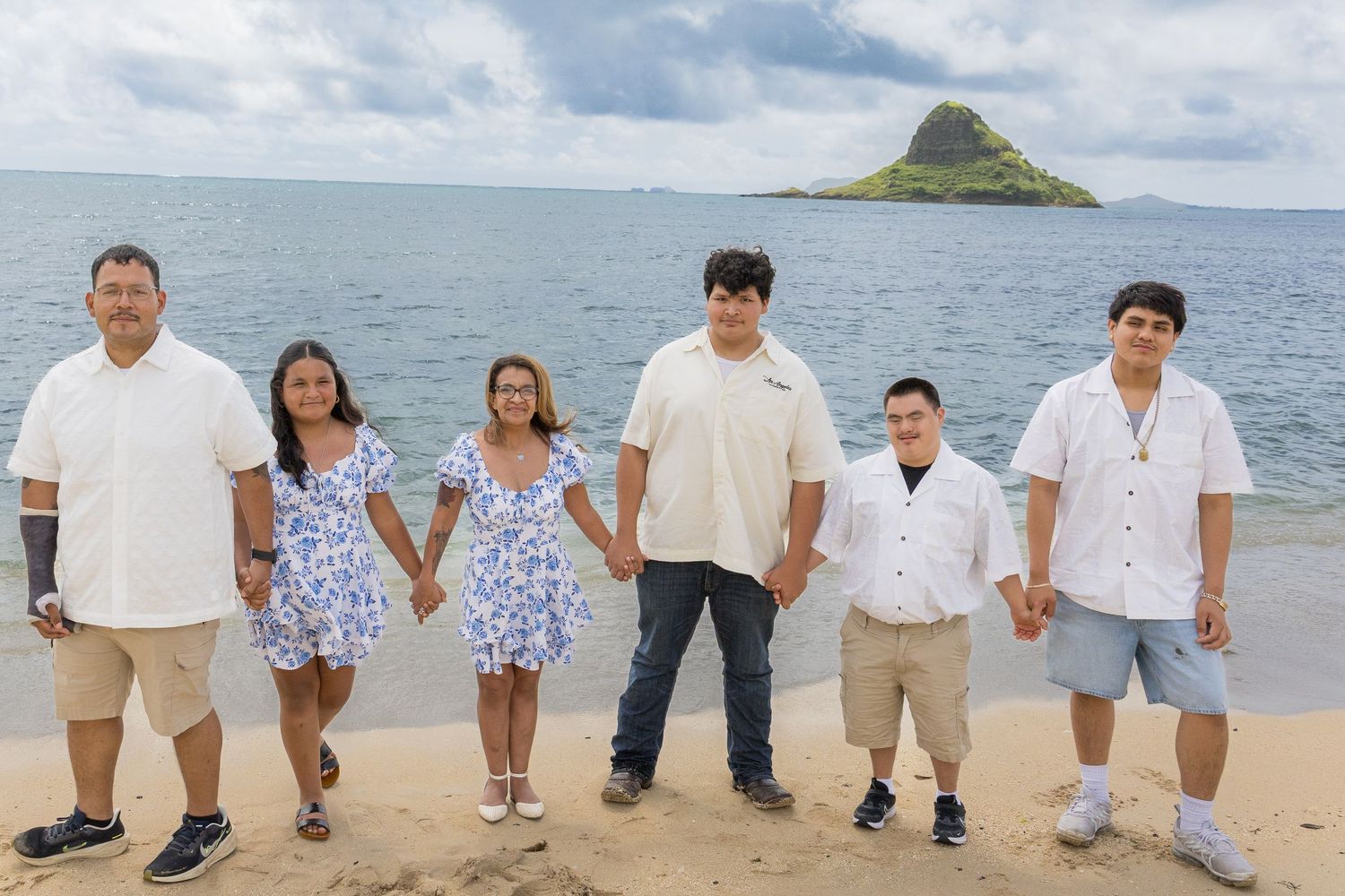 Family of six posing on a sandy beach with Chinaman's Hat island in the background, Hawaii.