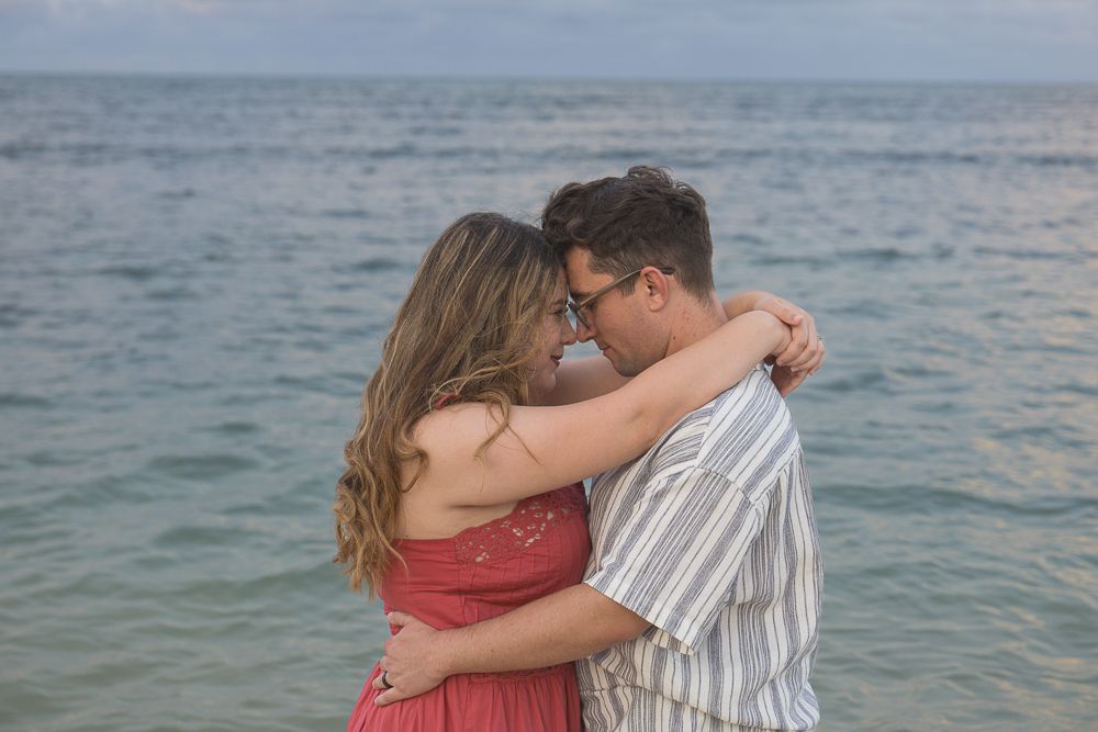 Romantic couple embracing and touching foreheads on calm ocean beach in soft evening light.