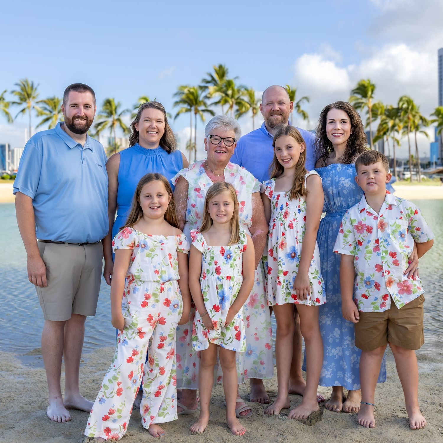 Family of nine posing on a tropical beach in Hawaii with palm trees and ocean in the background.