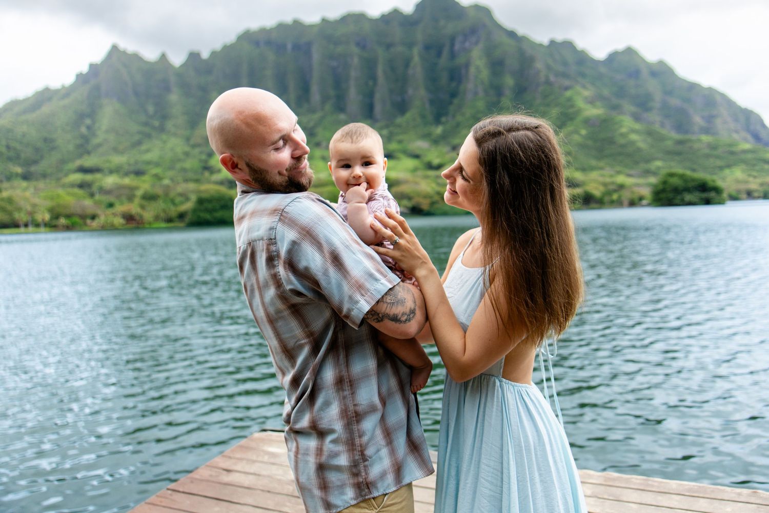 Happy family with baby on wooden dock with stunning Hawaii mountain lake view.