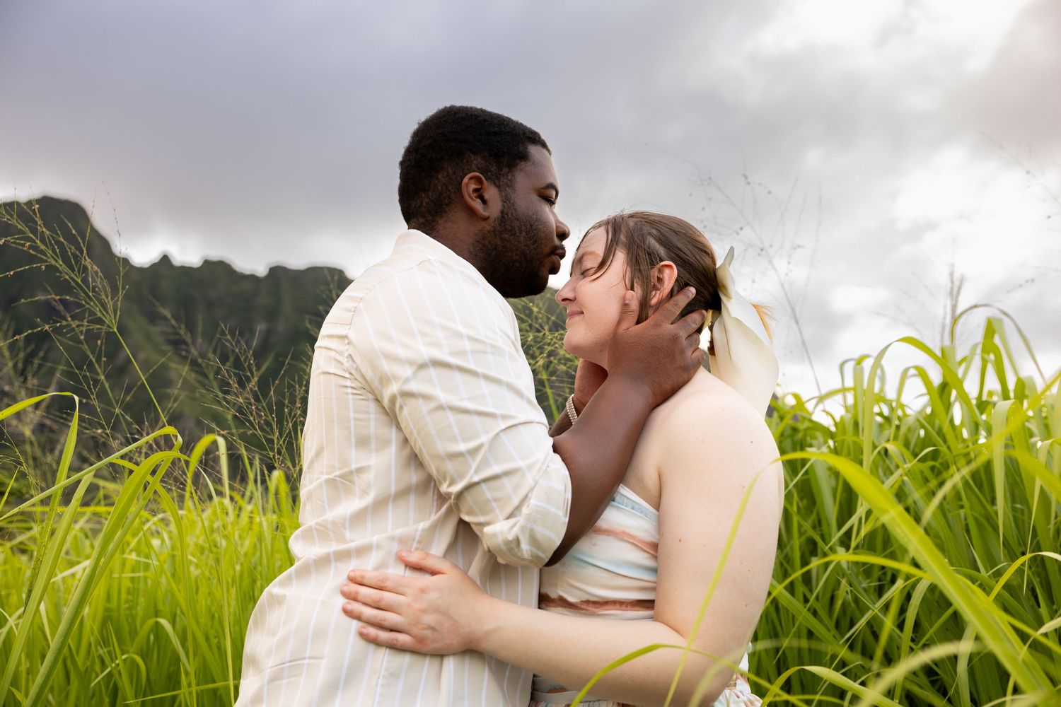 Loving interracial couple embracing and almost kissing surrounded by tall green grass in Hawaii.