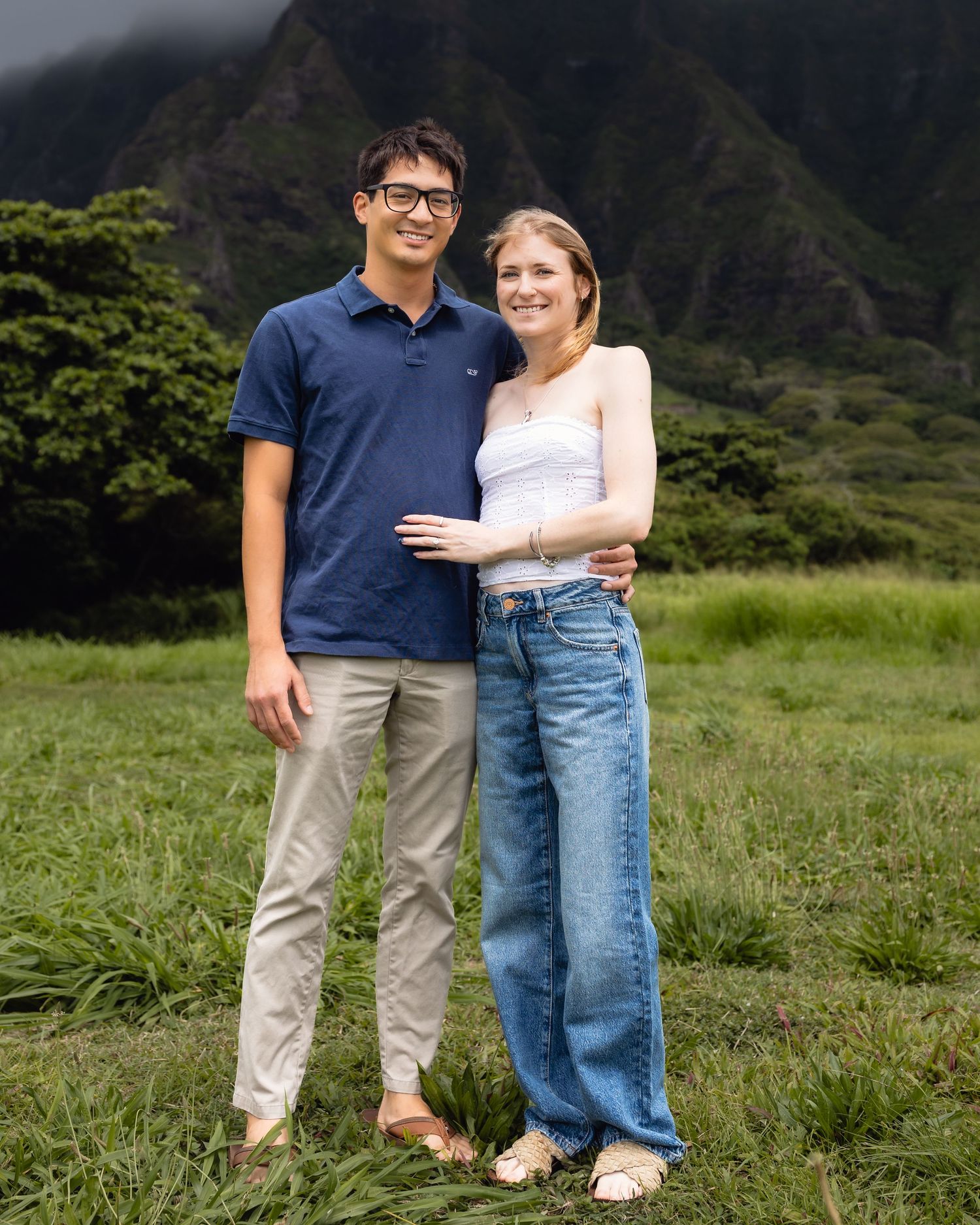Couple posing together in a lush green field with dramatic mountain backdrop in Hawaii.