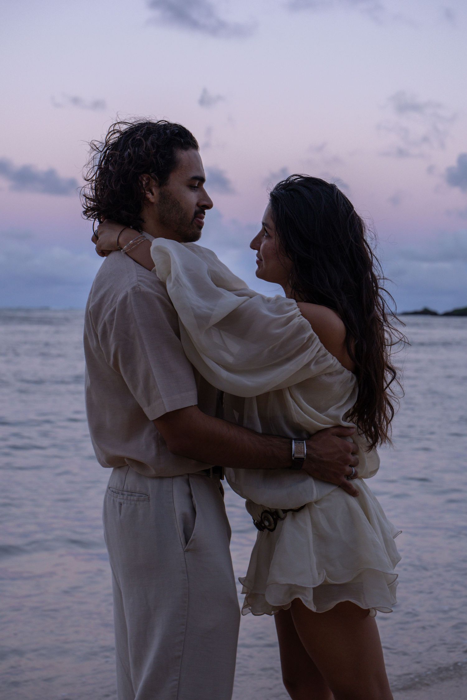 Romantic couple embraces on beach during stunning pink and purple sunset.