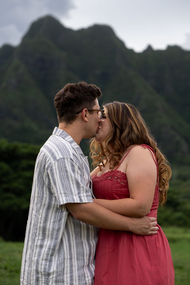 Couple sharing romantic kiss with dramatic green mountain landscape in background outdoors.