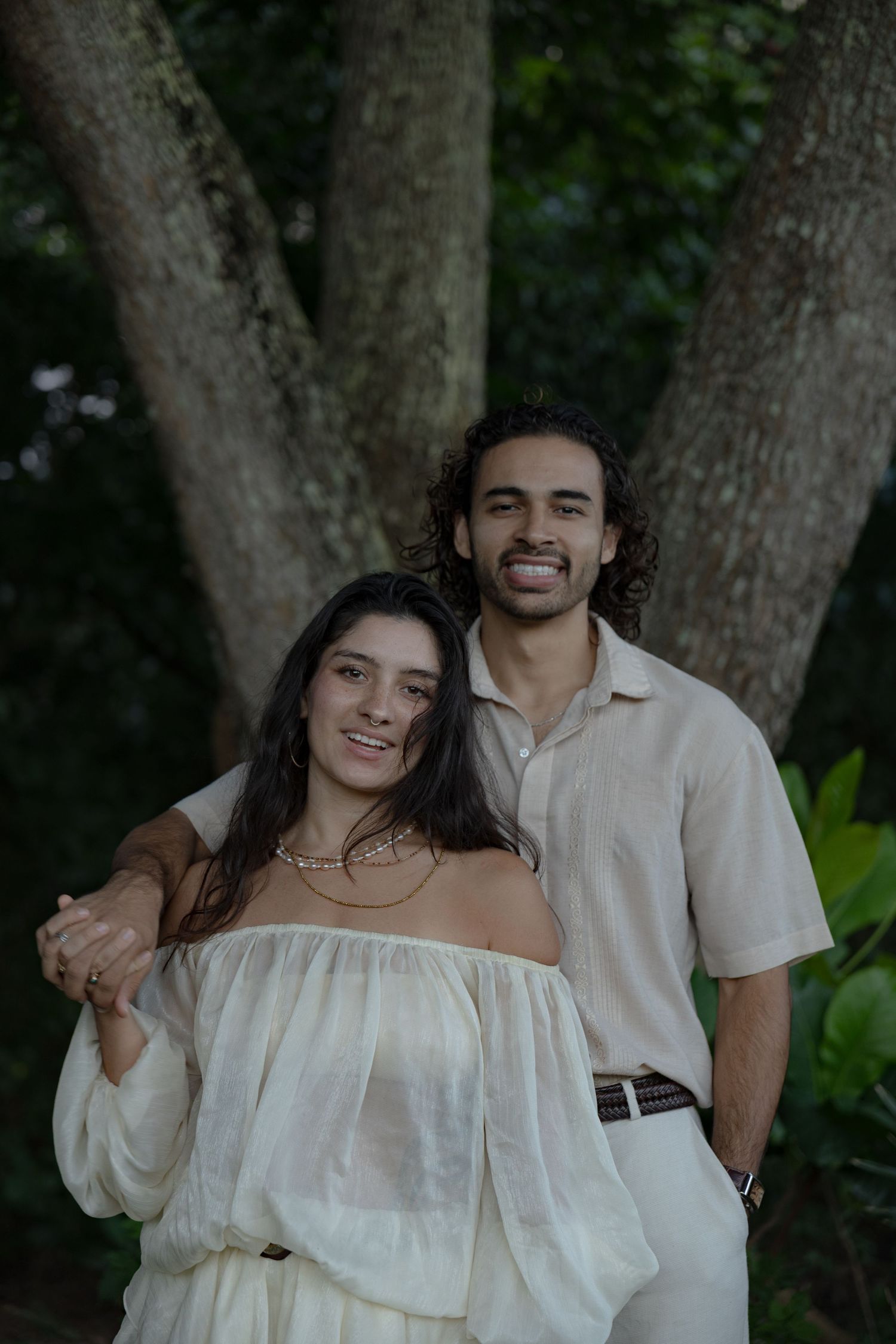 Smiling couple posing together under large tree in lush tropical setting.