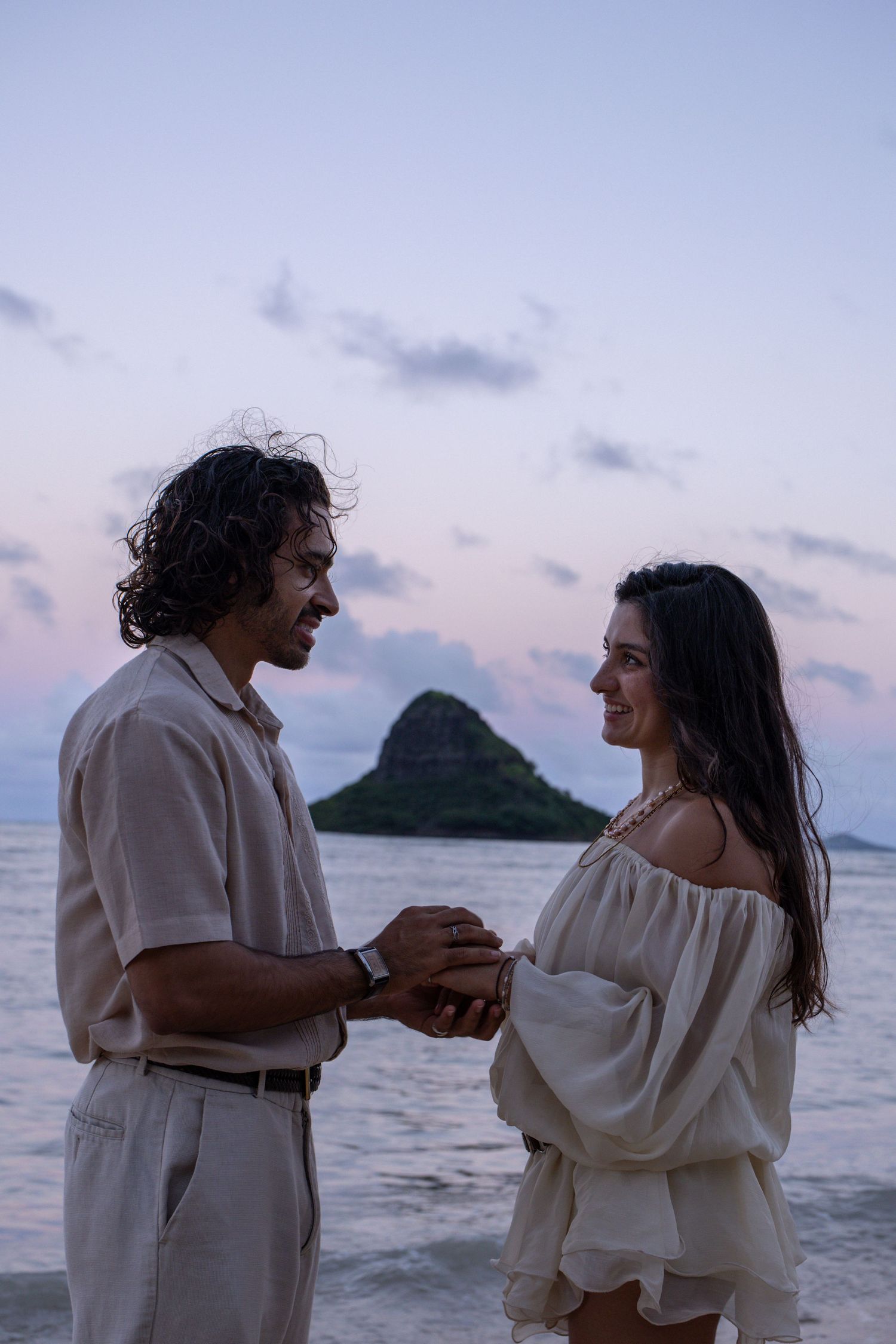 Couple holding hands on Hawaii beach with Mokolii island at twilight.