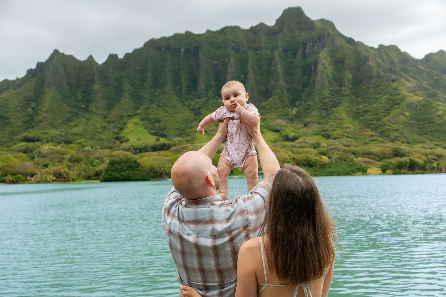 Father lifting baby above head with mother watching at Hawaii mountain lake.