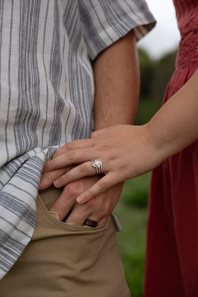 Close-up of a couple holding hands outdoors, the woman wearing a sparkling engagement and wedding ring set.