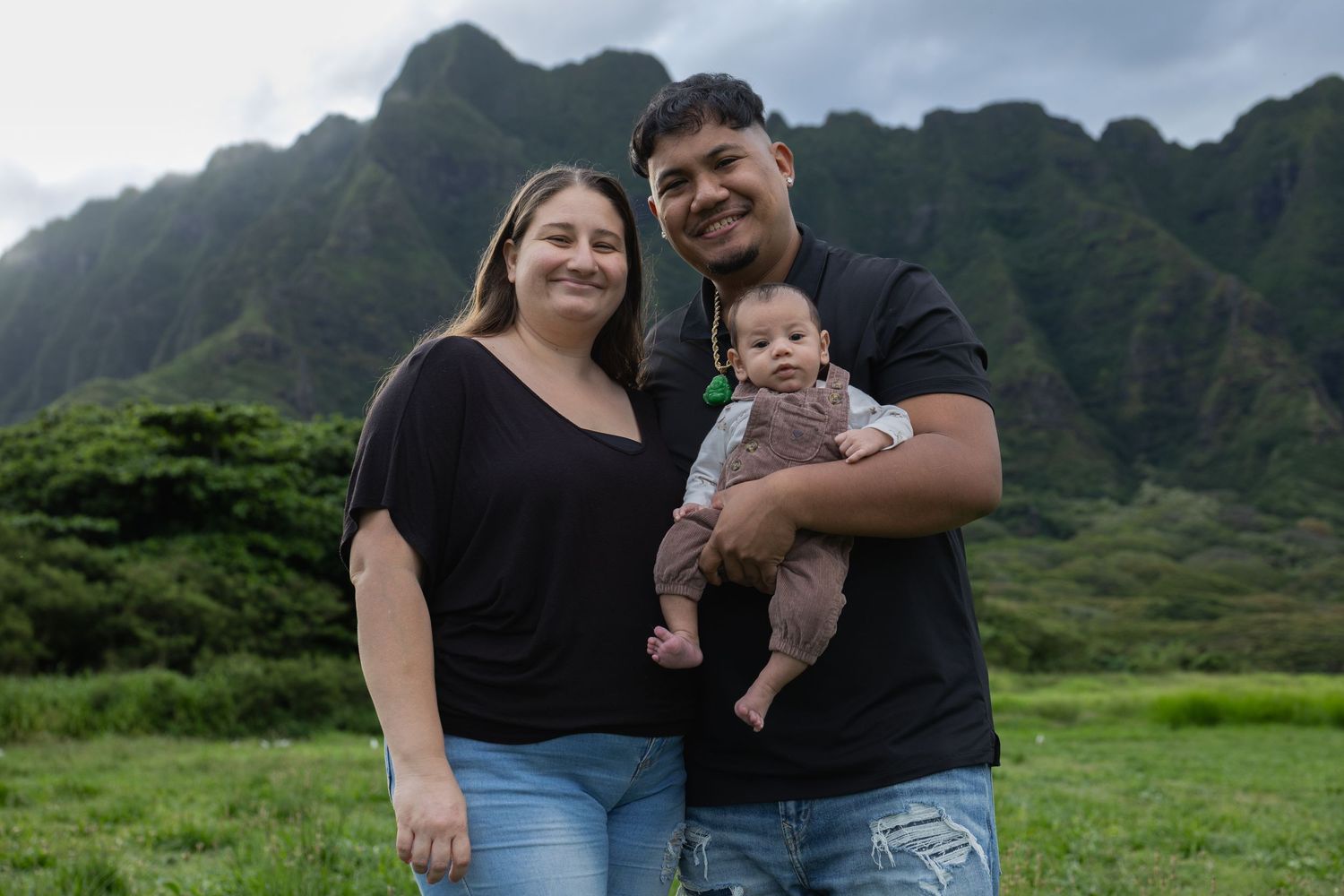 Happy family with baby posing in front of dramatic green mountains in Hawaii.