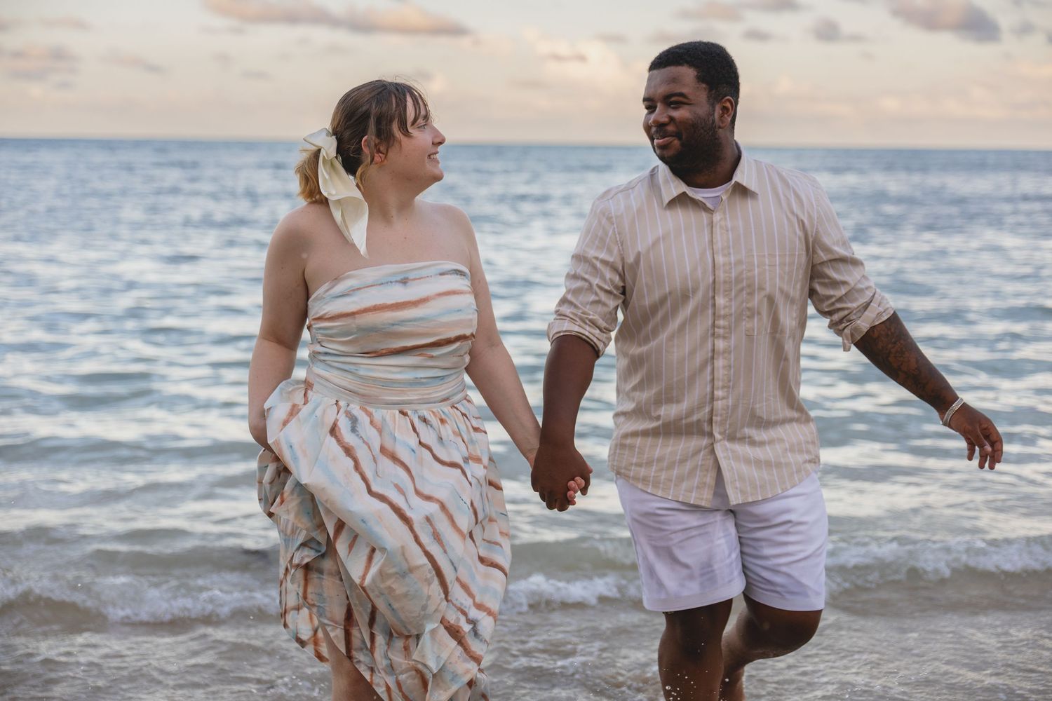 Happy couple holding hands and walking along a tropical beach at sunset in the ocean waves.