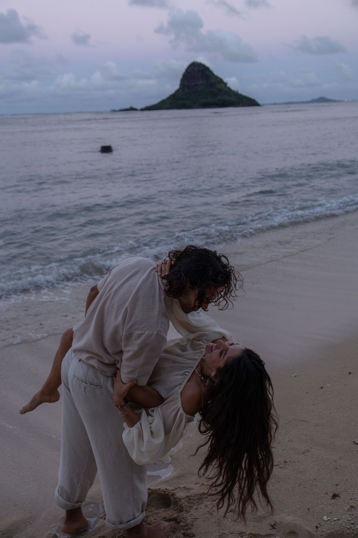 Couple dancing on beach at dusk with Chinaman Hat island visible in the background.