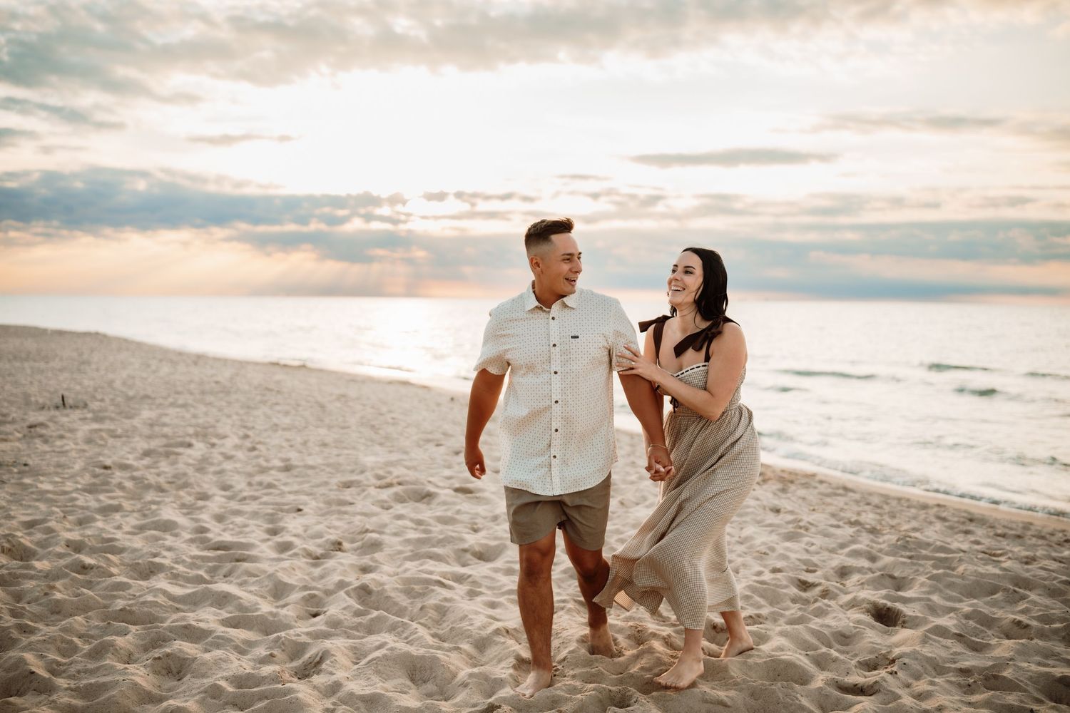 Couple walking hand-in-hand on a sandy beach at sunset, smiling and enjoying a romantic stroll by the ocean.