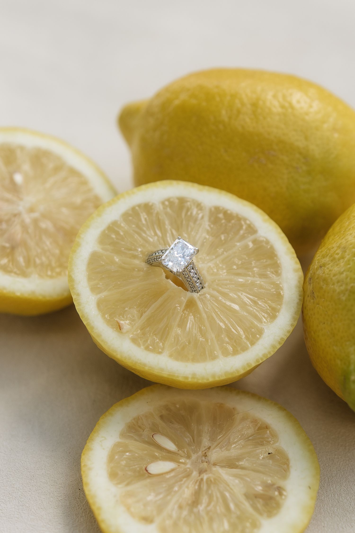 Diamond engagement ring displayed on a halved lemon surrounded by whole lemons on a light background.