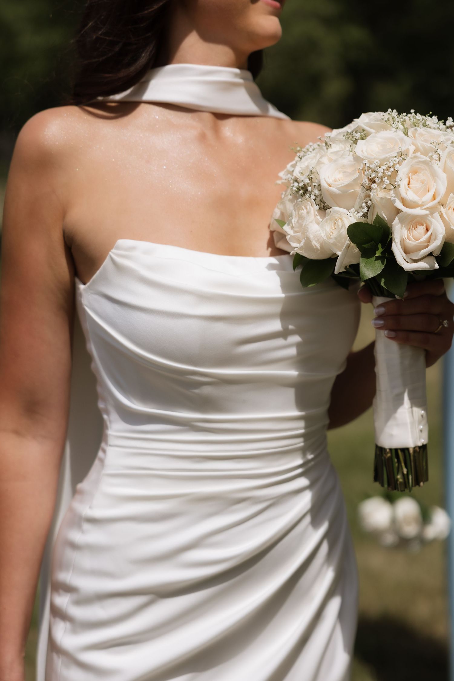 Close-up of bride in strapless halter gown holding white rose and baby breath bouquet.