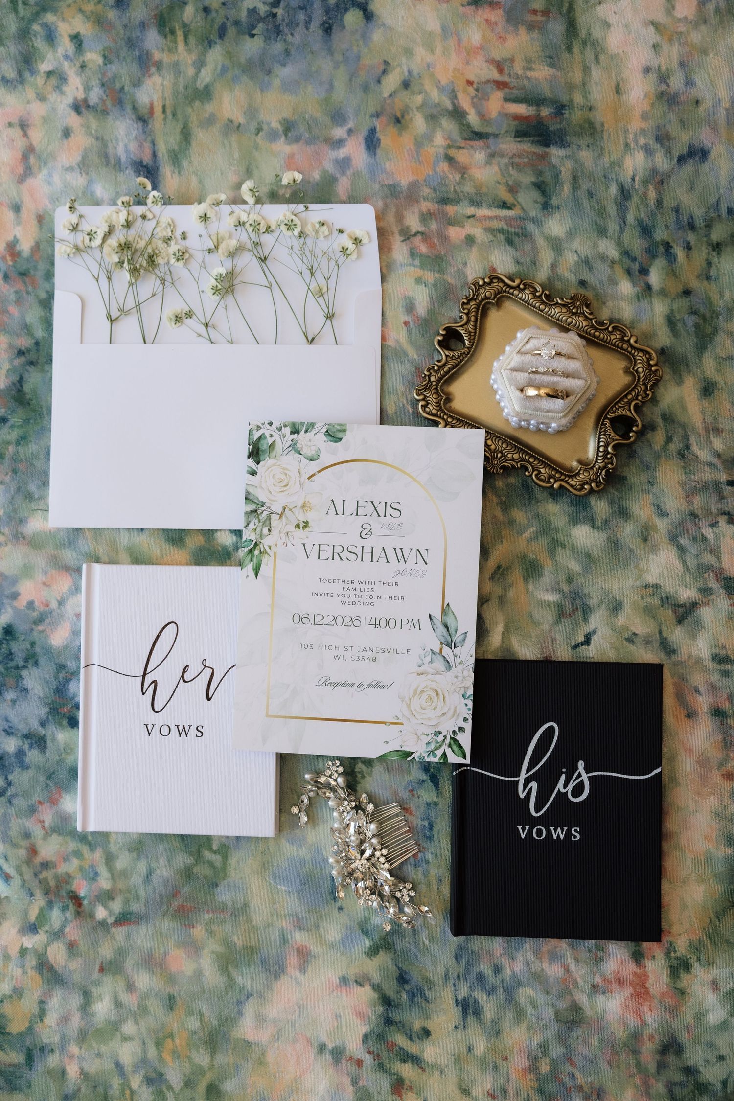 Elegant wedding flat lay featuring his and her vow books, floral invitation suite, gold ring dish, and baby's breath accents.