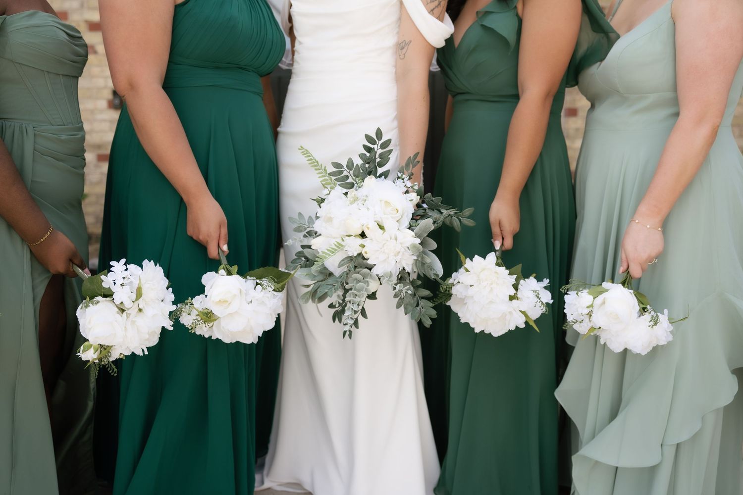 Bride in white gown with bridesmaids in green dresses holding white peony and eucalyptus bouquets.
