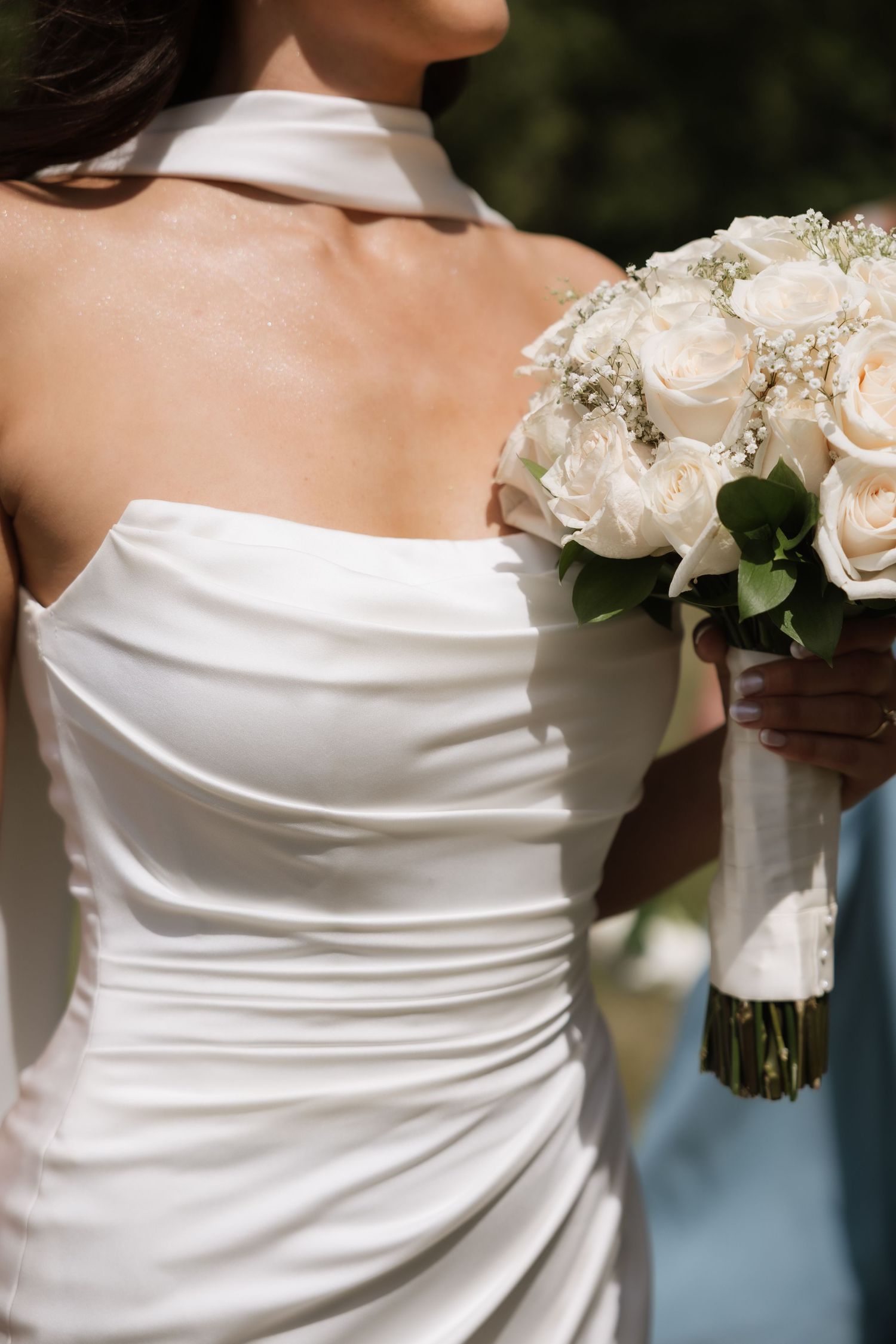 Bride in a strapless white satin wedding gown holding an elegant bouquet of white roses and baby's breath.