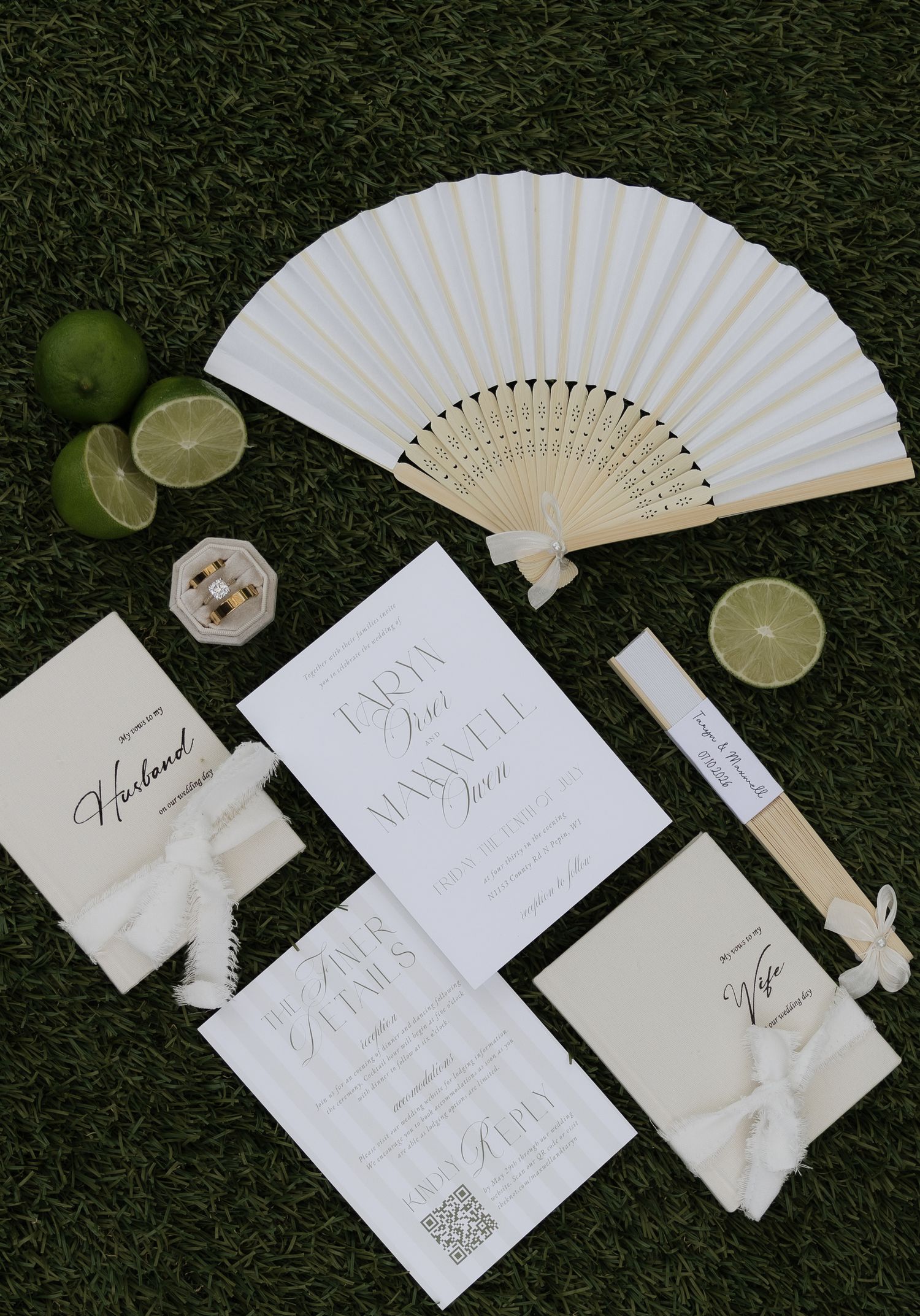 Elegant white wedding stationery suite with fan, limes, and ribbon on green grass.
