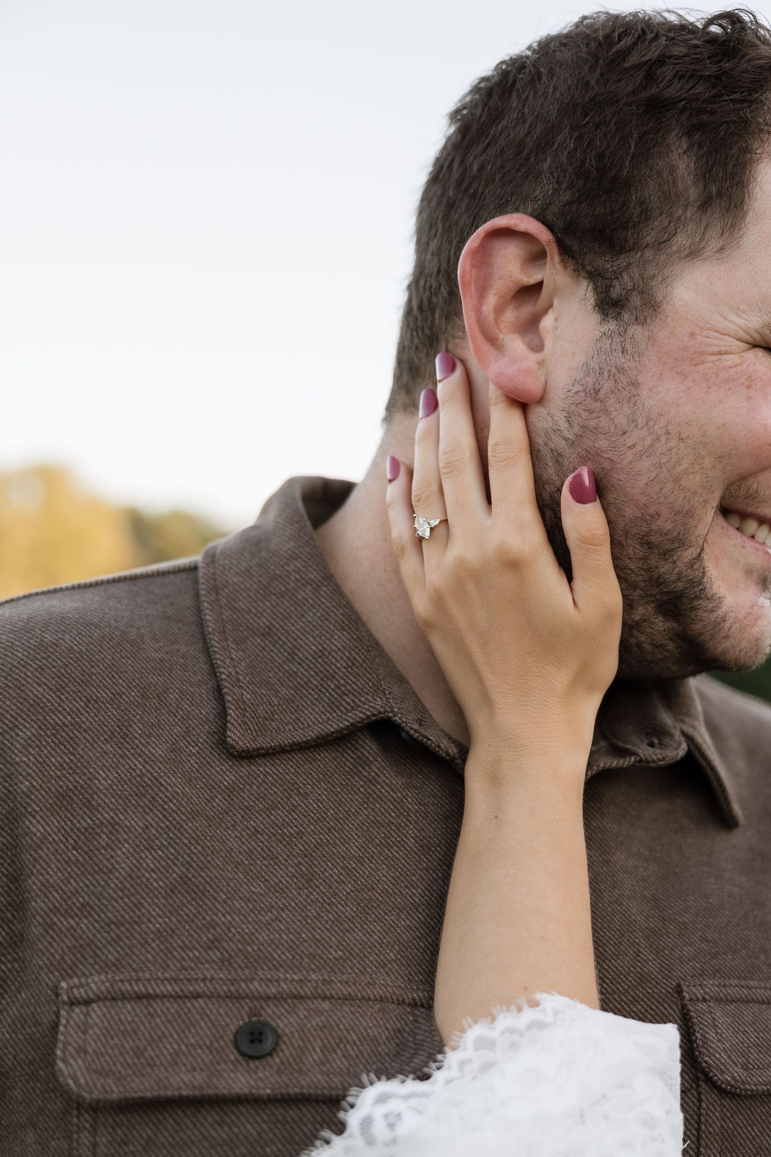Woman with engagement ring and purple nails tenderly touches smiling bearded mans face outdoors in autumn.
