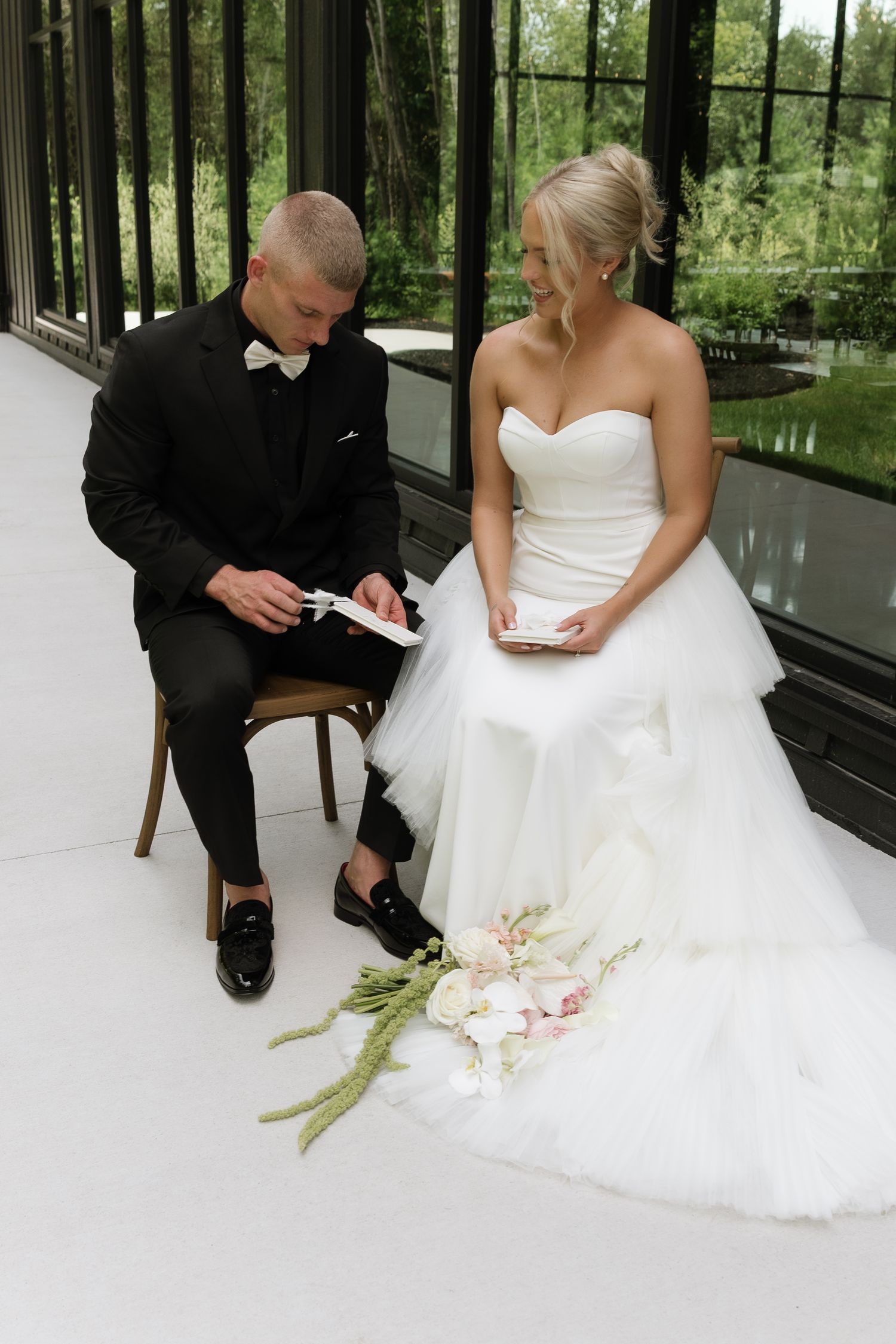 Bride and groom in wedding attire reading vows in a glass conservatory with lush garden views.