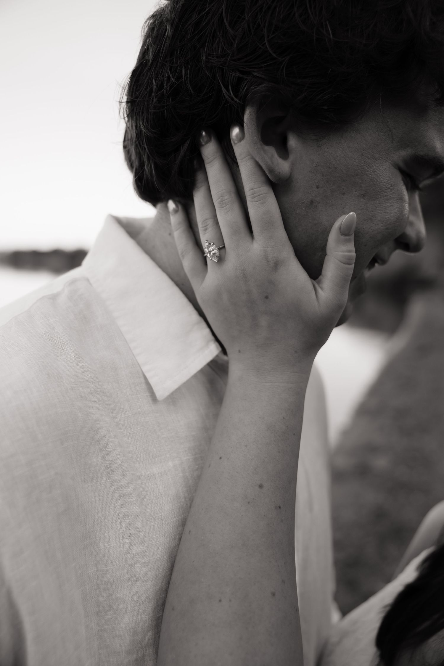 Black and white photo of a woman tenderly touching a mans face, showcasing her diamond engagement ring.