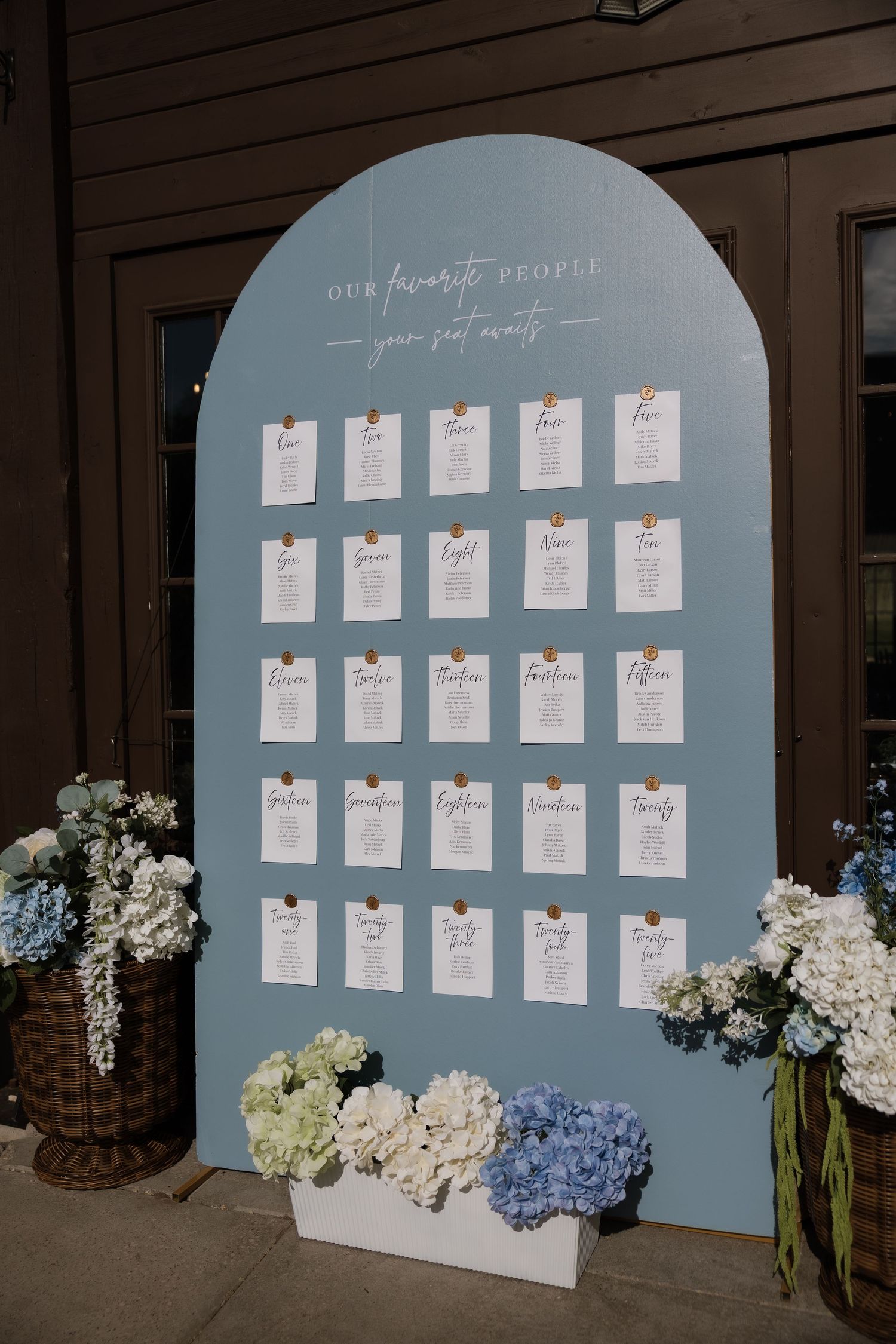 Blue arched wedding seating chart display with white cards and hydrangea flowers at venue entrance.