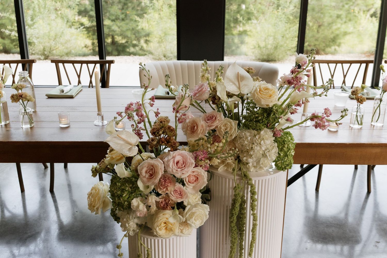 Elegant wedding reception table with lush floral arrangement featuring blush roses, white blooms, and greenery on a ribbed white vase.