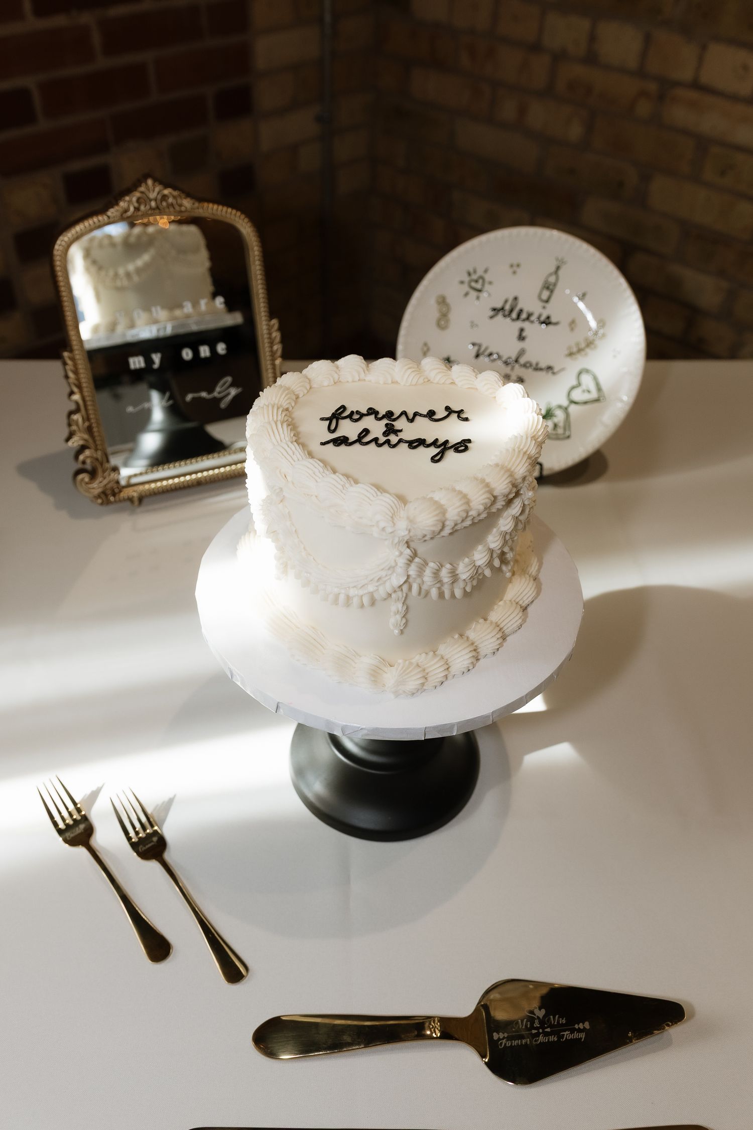 White heart-shaped wedding cake inscribed with forever always on a cake stand, with gold forks and a cake server.
