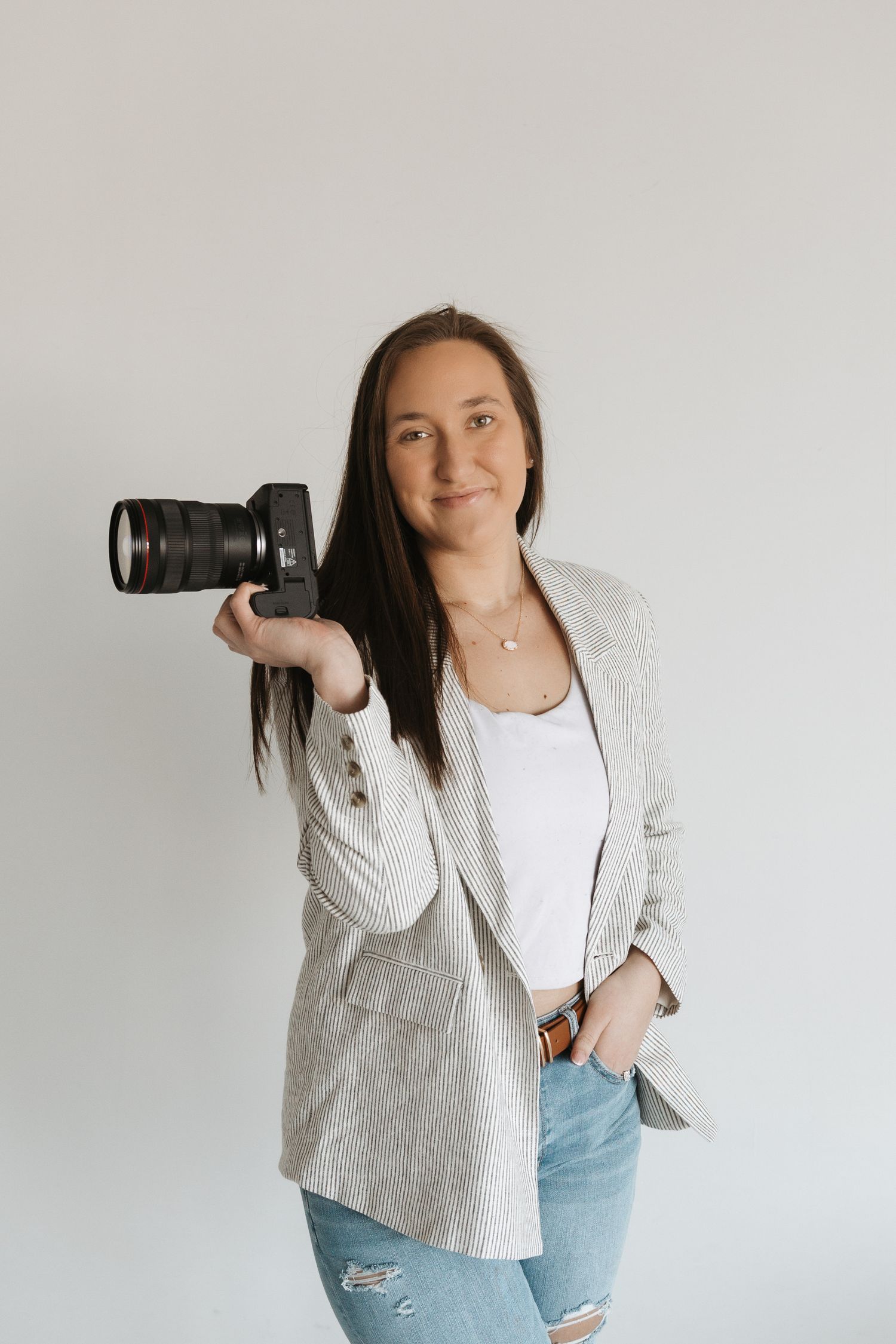 Professional female photographer smiling and holding a DSLR camera against a white background.