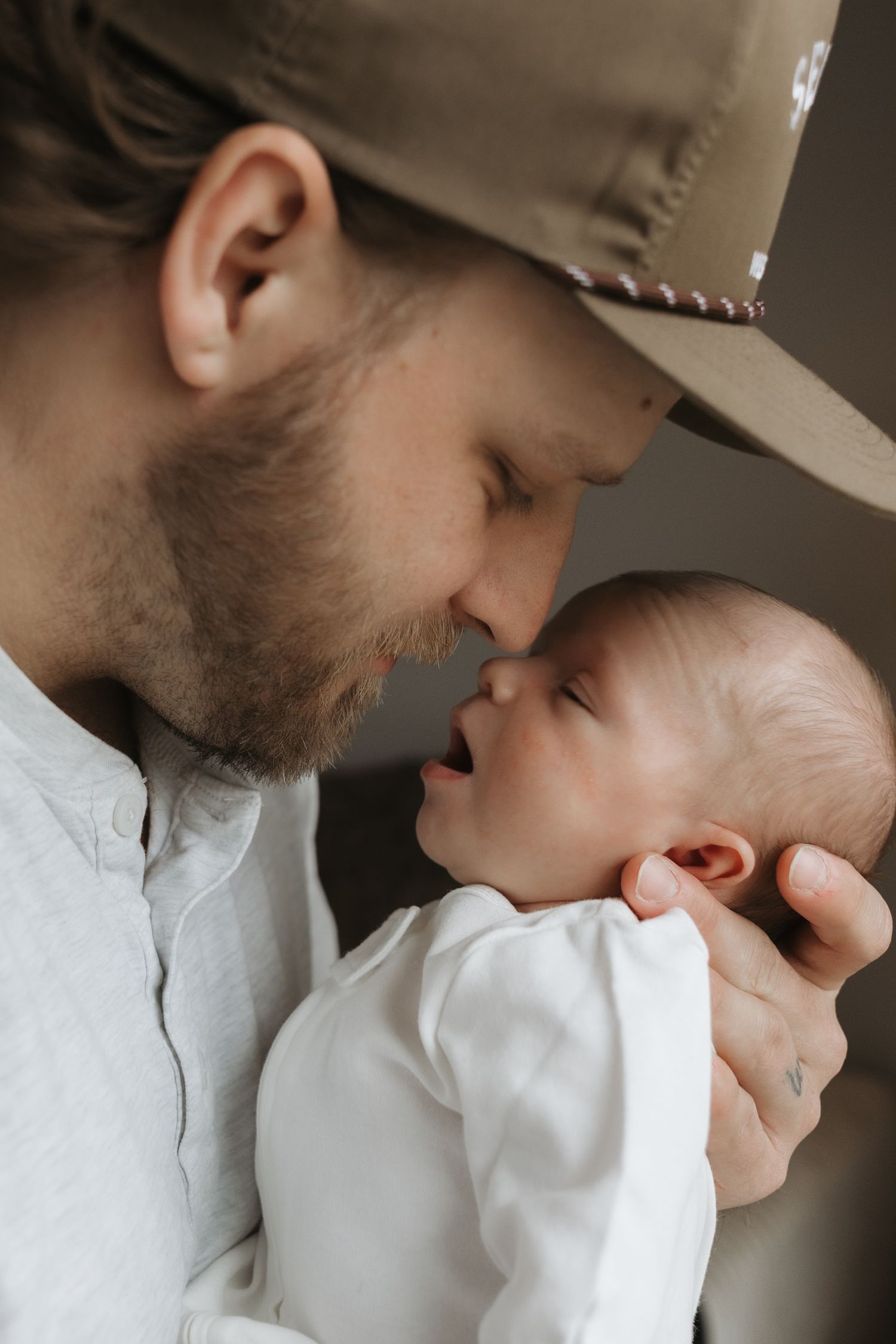 A bearded father in a tan hat touching noses with his newborn baby.