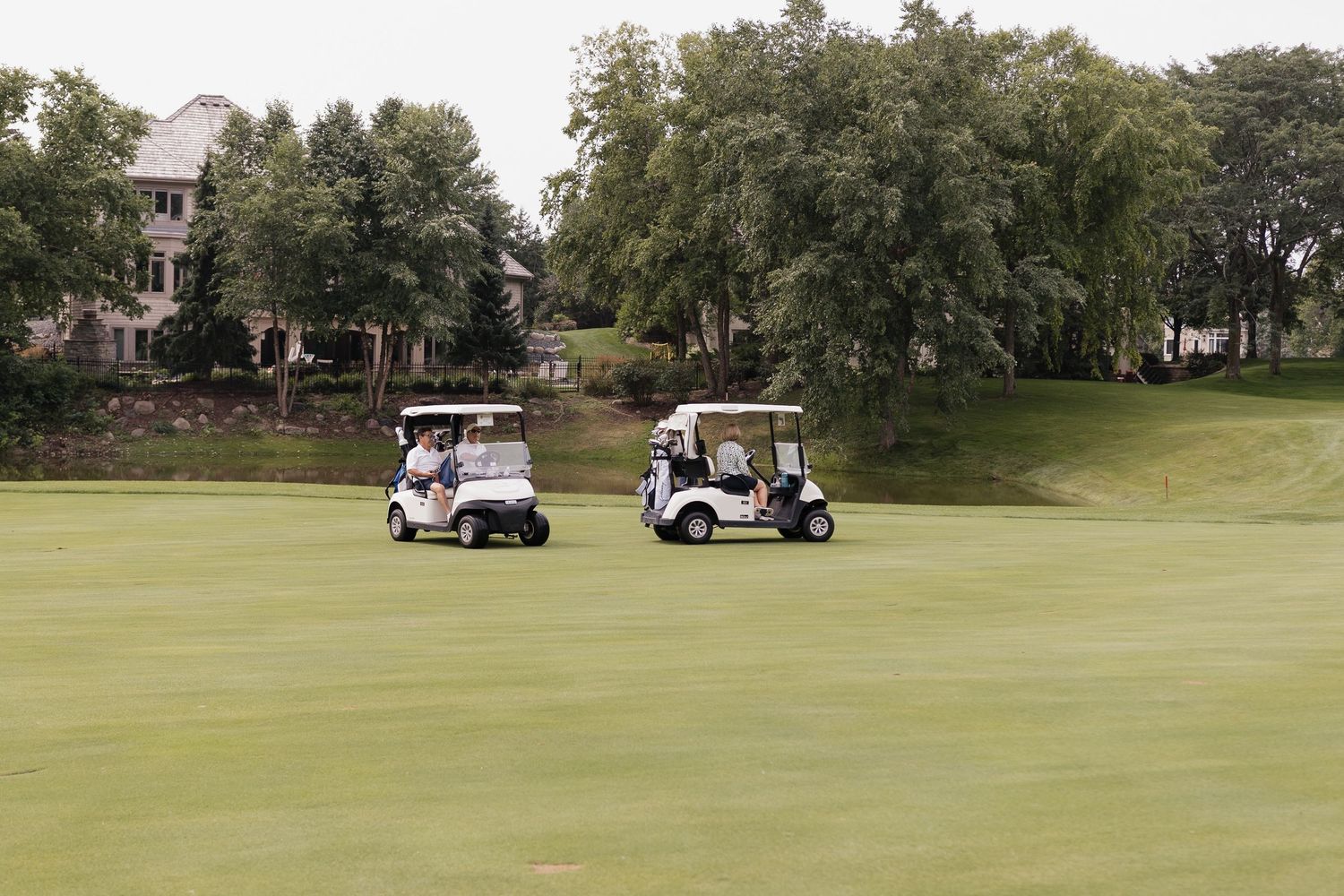 Two white golf carts driving on a lush green golf course fairway surrounded by trees.
