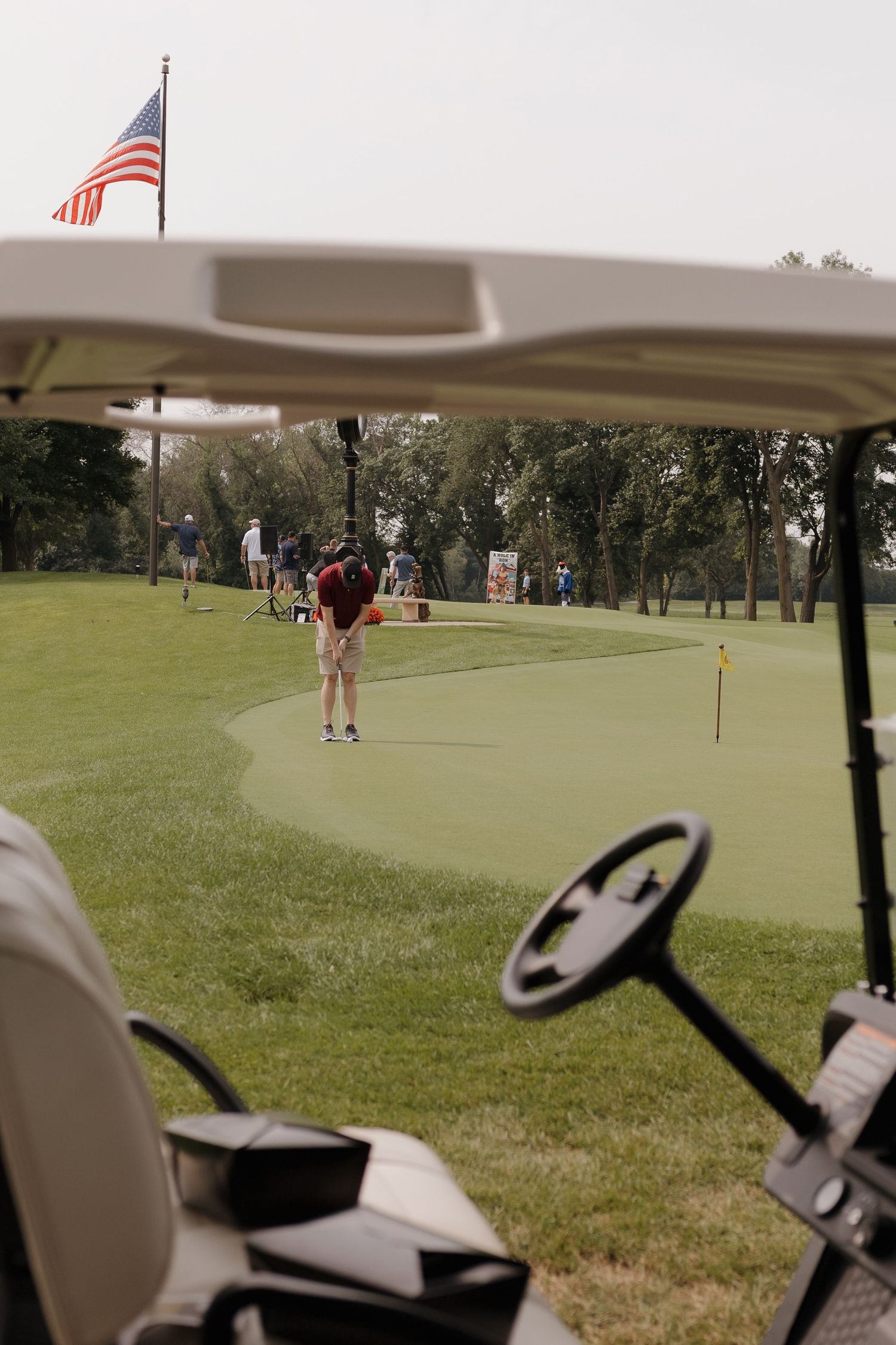 Golfer putting on a green golf course with a golf cart and American flag in the foreground.