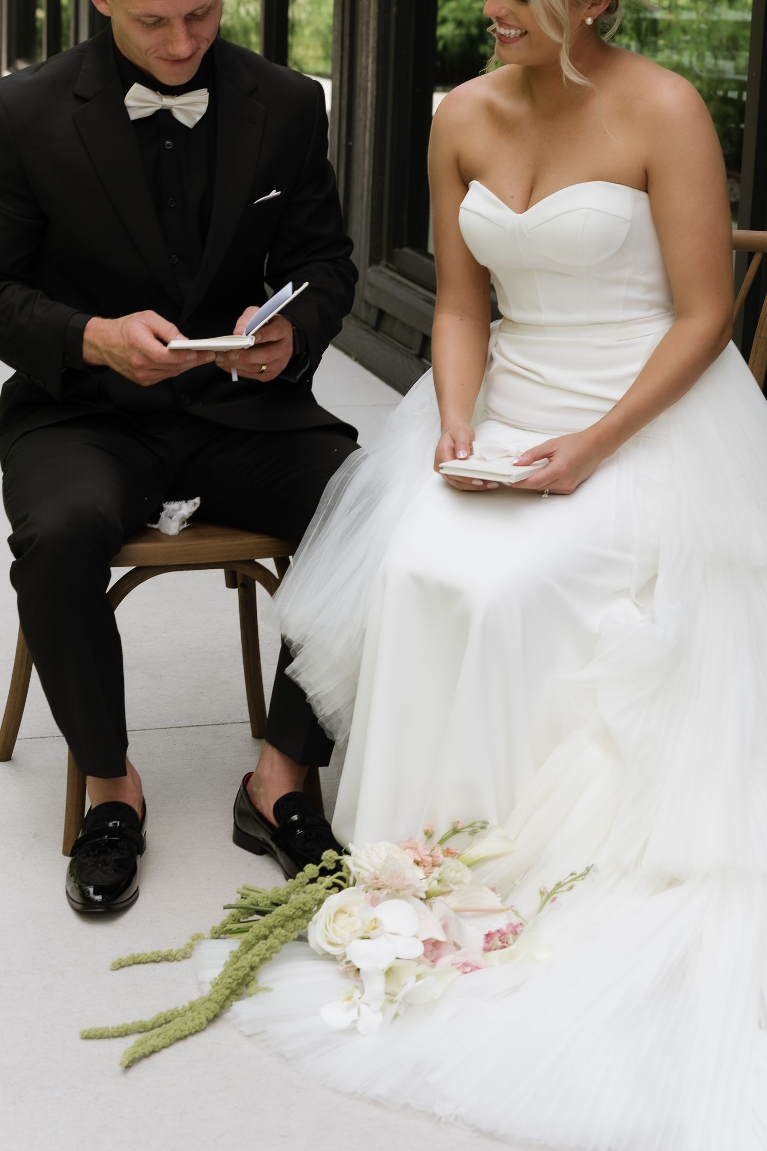 Bride and groom reading vows from cards during ceremony, bouquet of white and pink flowers on floor.