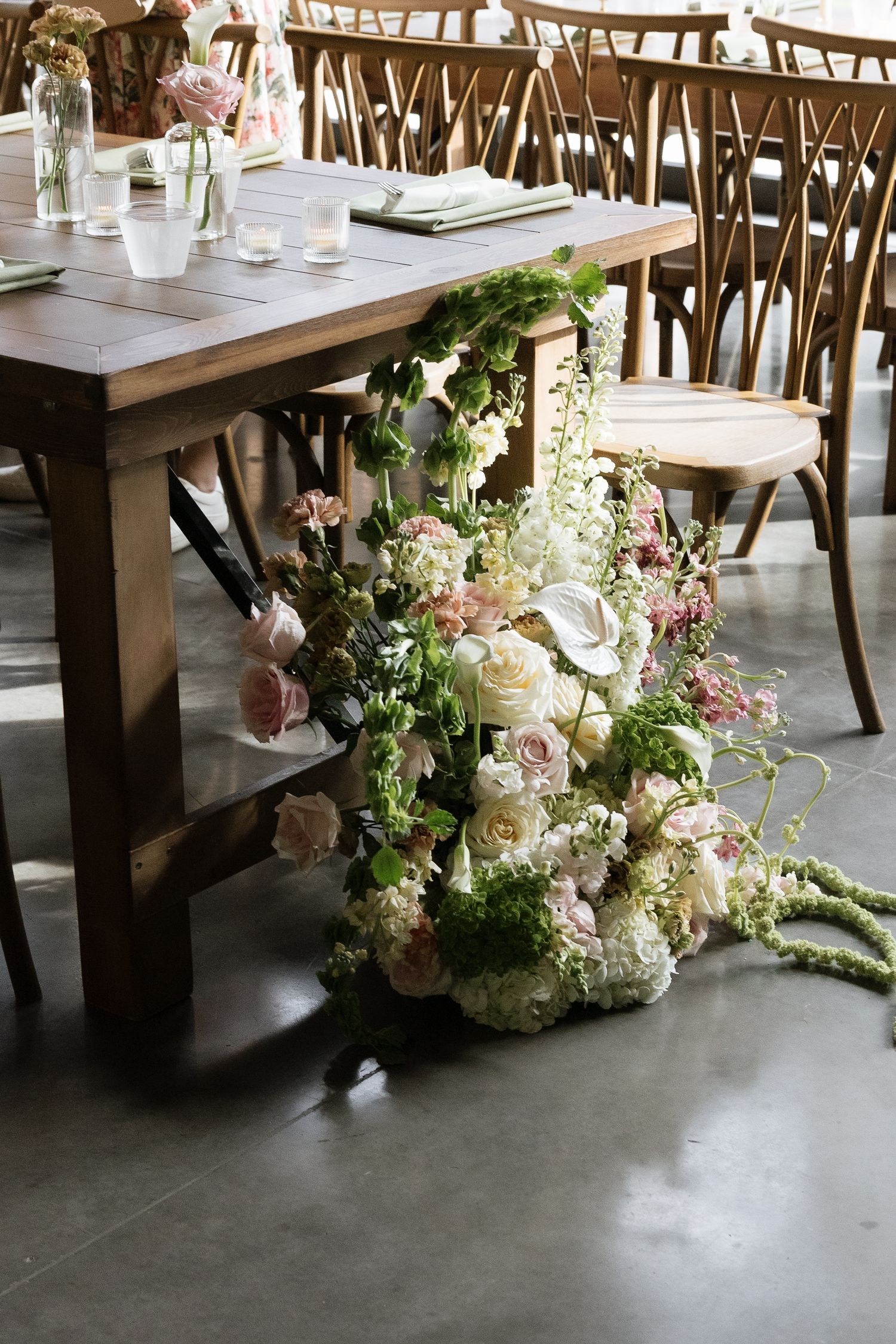 Elegant wedding reception table with cascading floral arrangement of white and pink roses spilling onto concrete floor.
