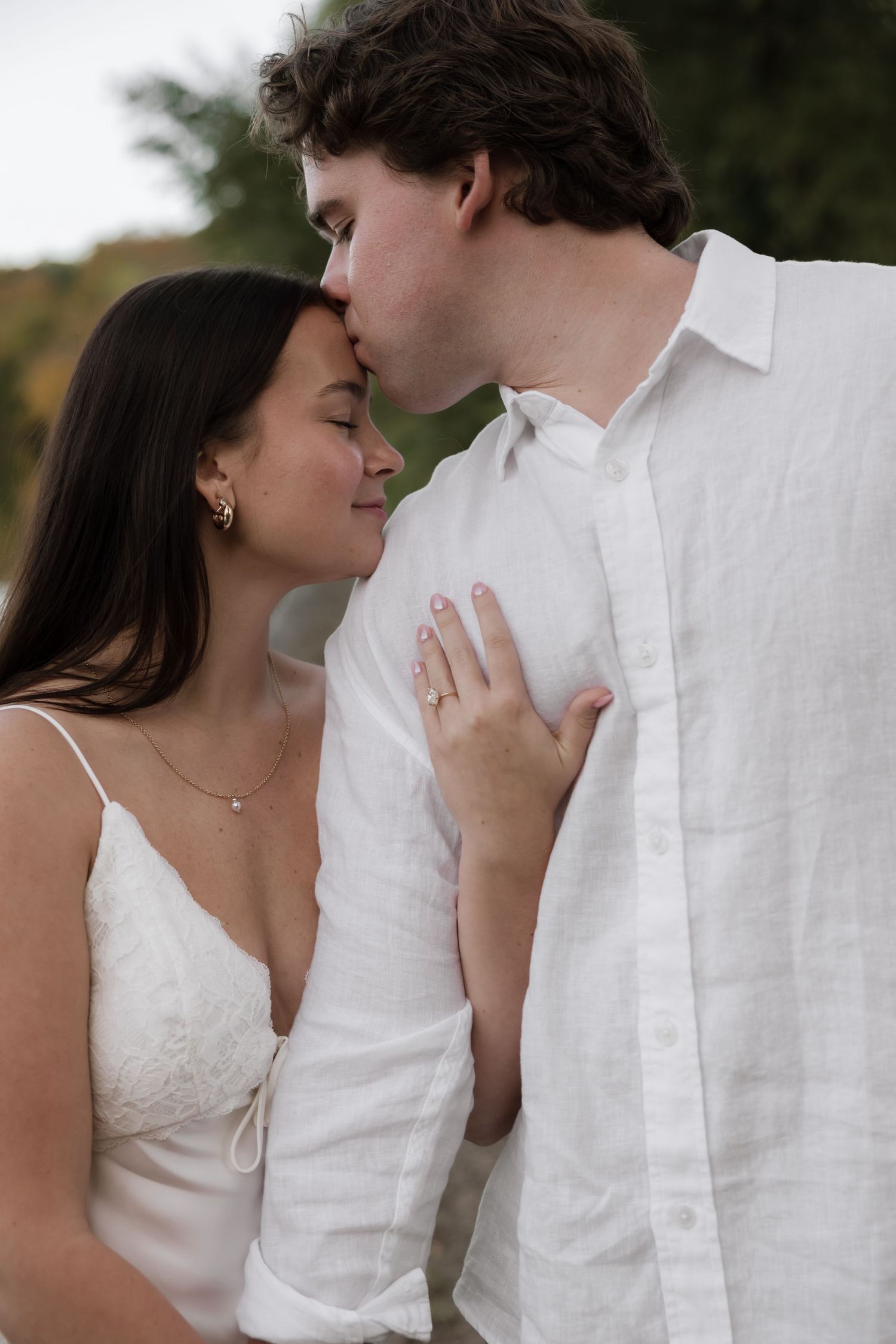 Romantic couple sharing a tender kiss, woman showing engagement ring while holding mans white shirt.