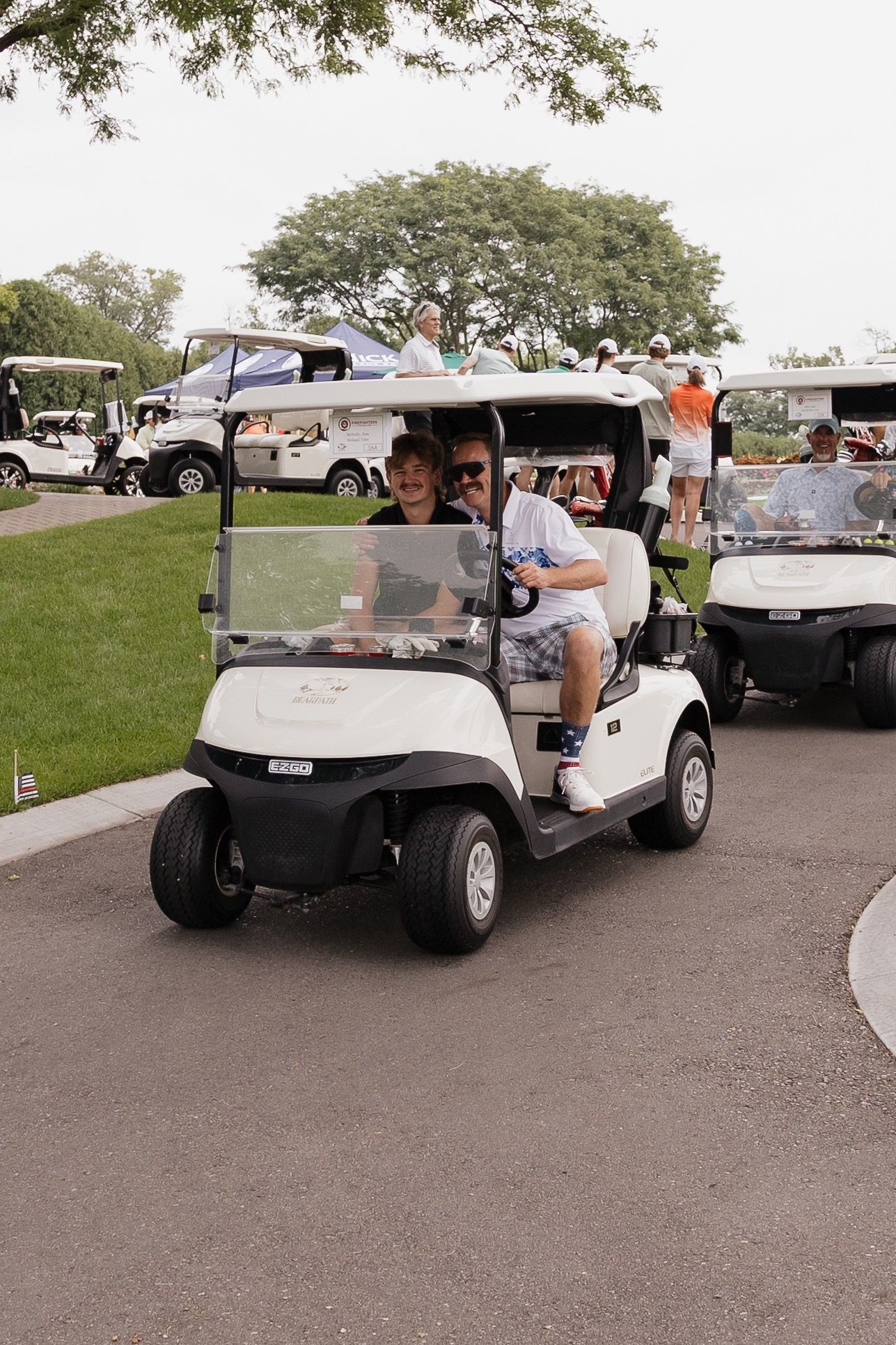 People riding a white golf cart on a paved path at a golf course during a sunny day.