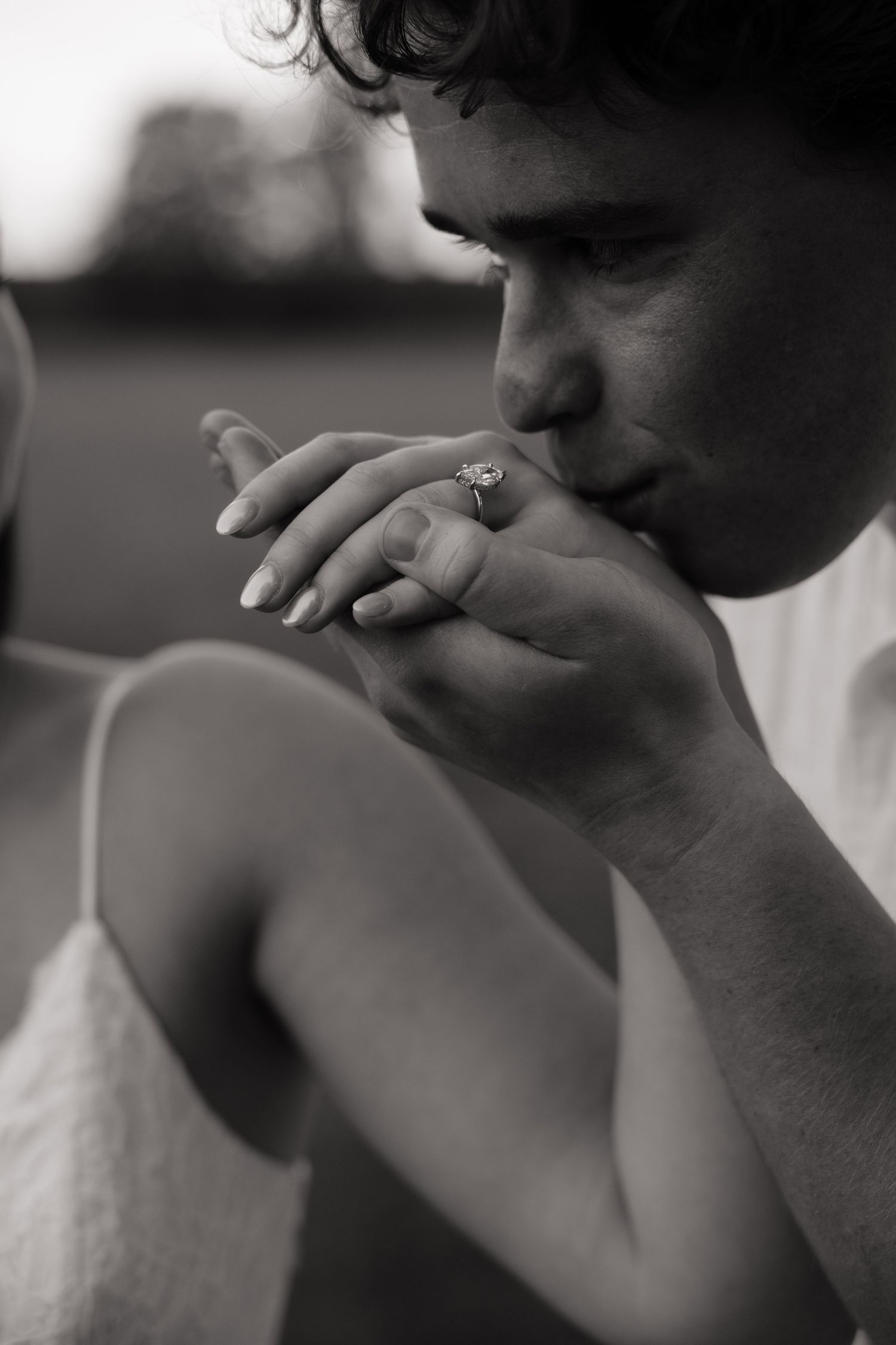 Black and white photo of groom kissing bride's hand adorned with a sparkling diamond engagement ring.