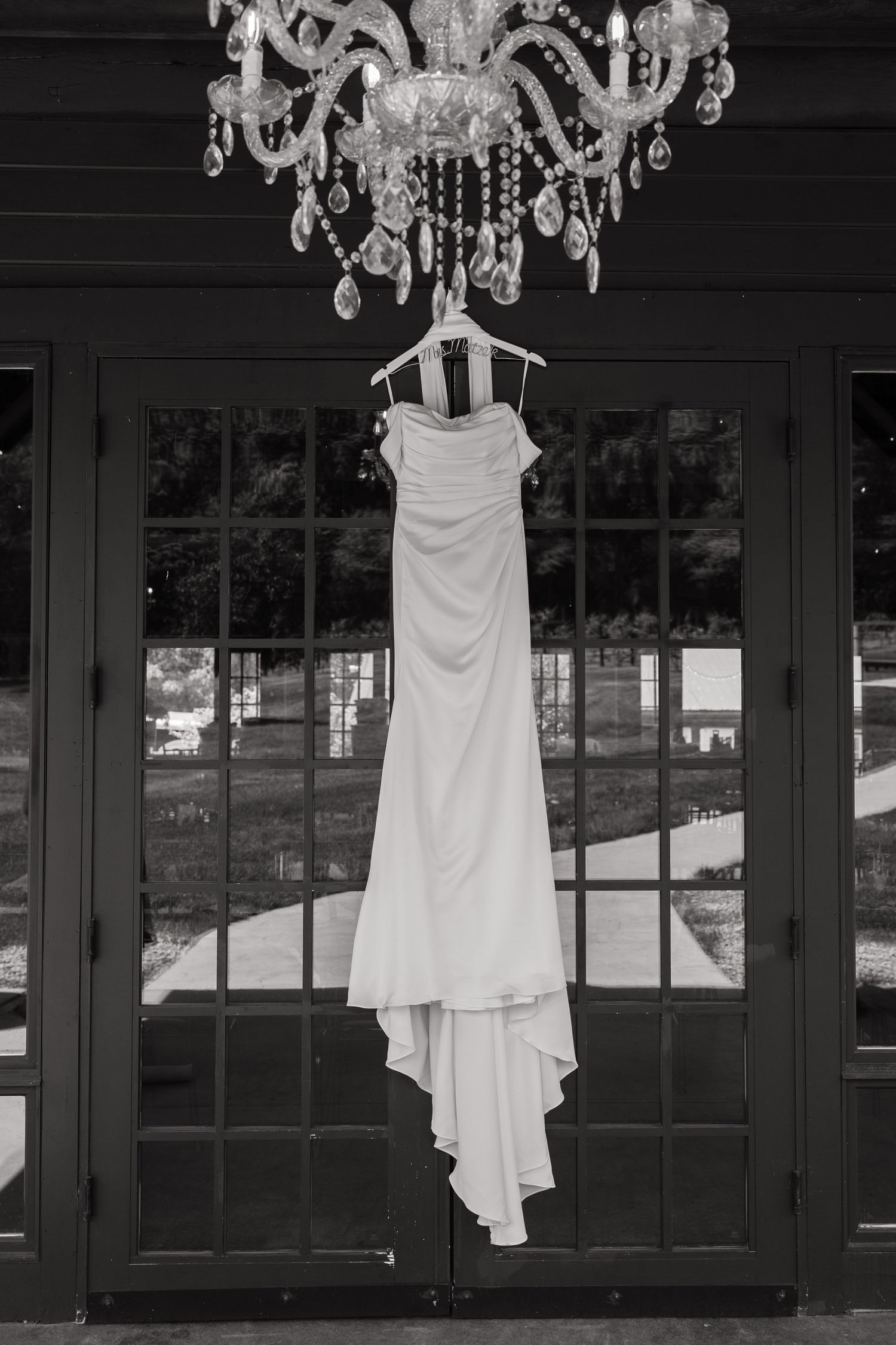 Black and white photo of a strapless wedding gown hanging from a crystal chandelier.